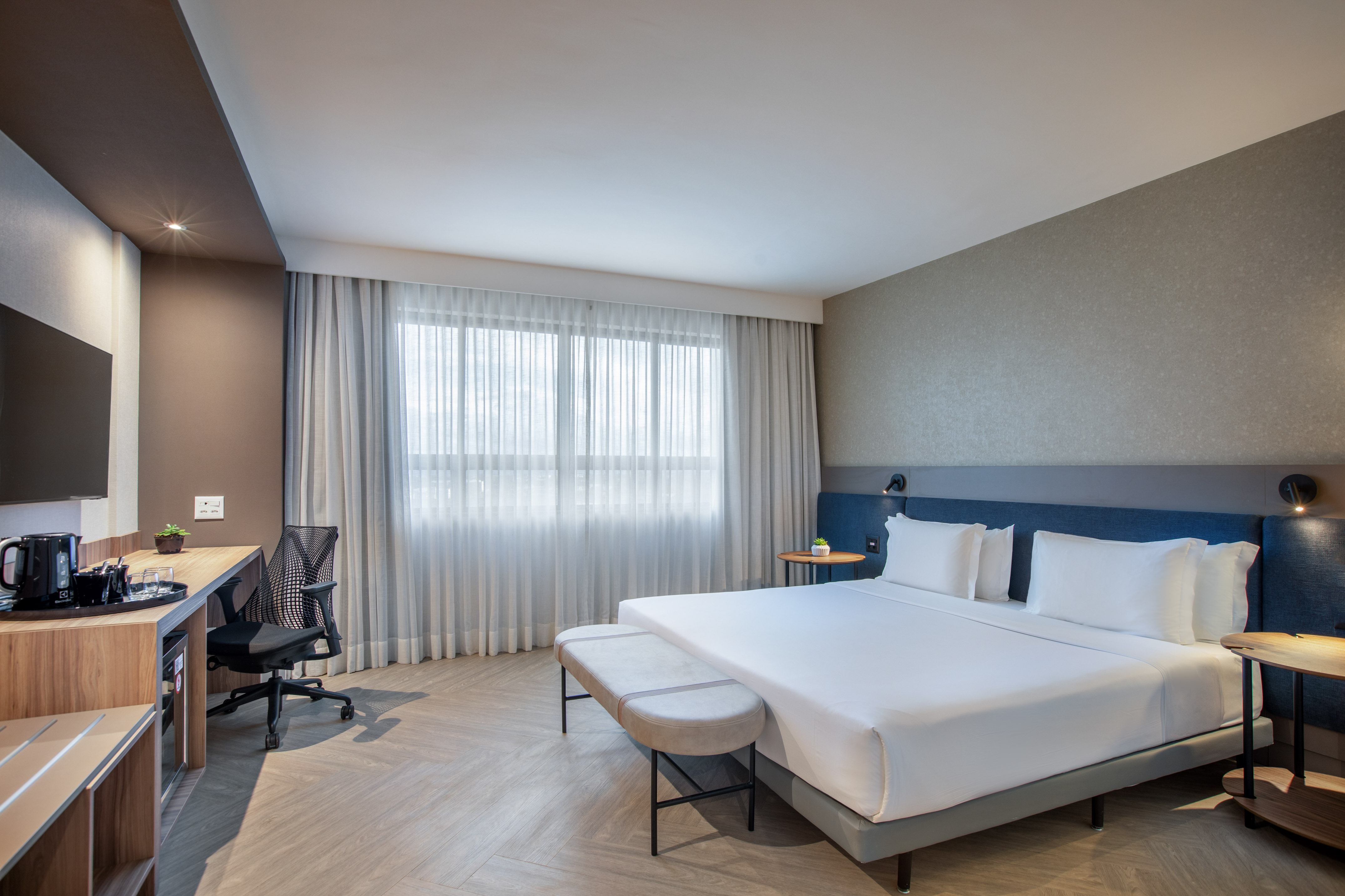 Modern hotel bedroom with king bed, work desk, and large window.