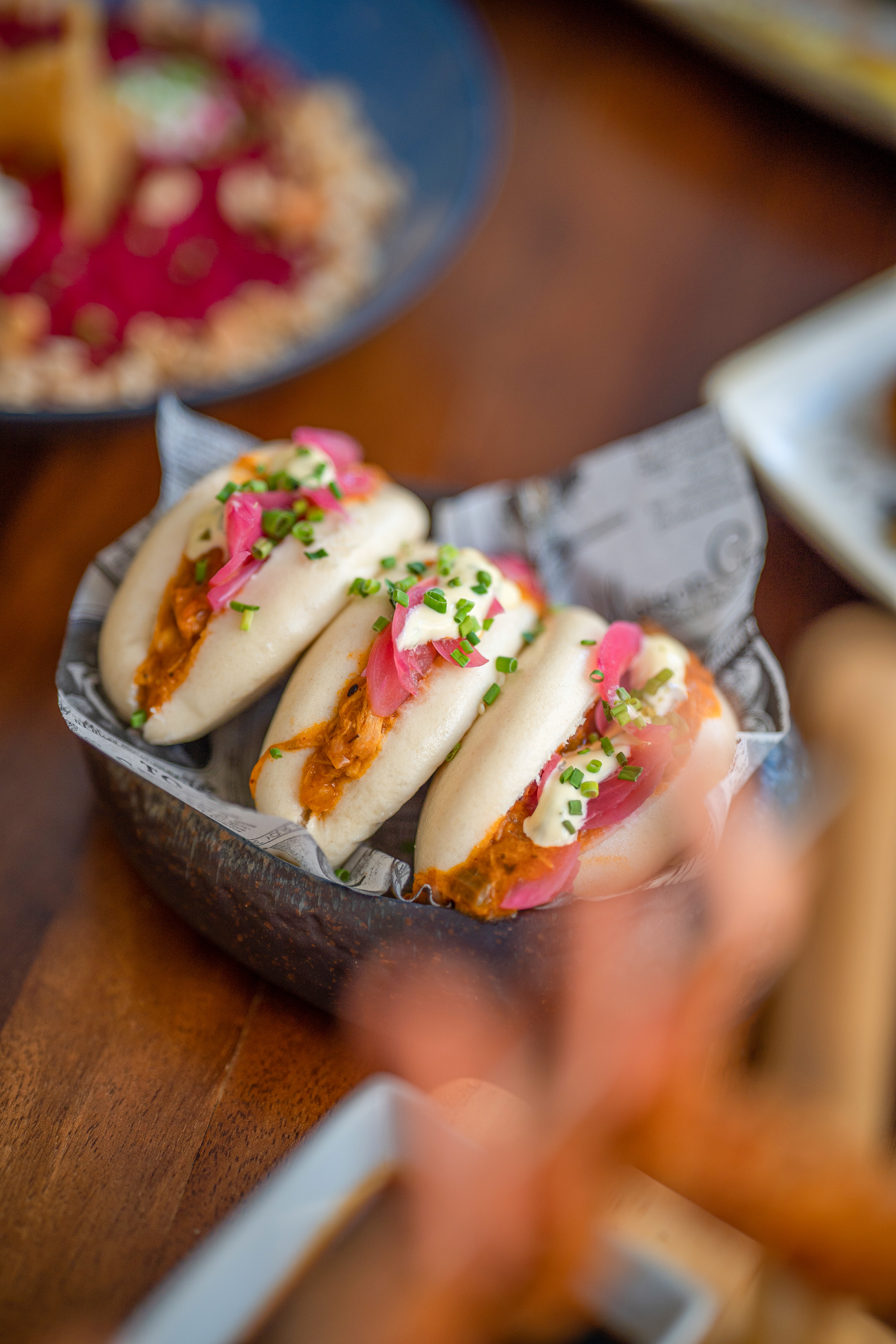 Three steamed bao buns with pulled pork, pickled onions, and chives.