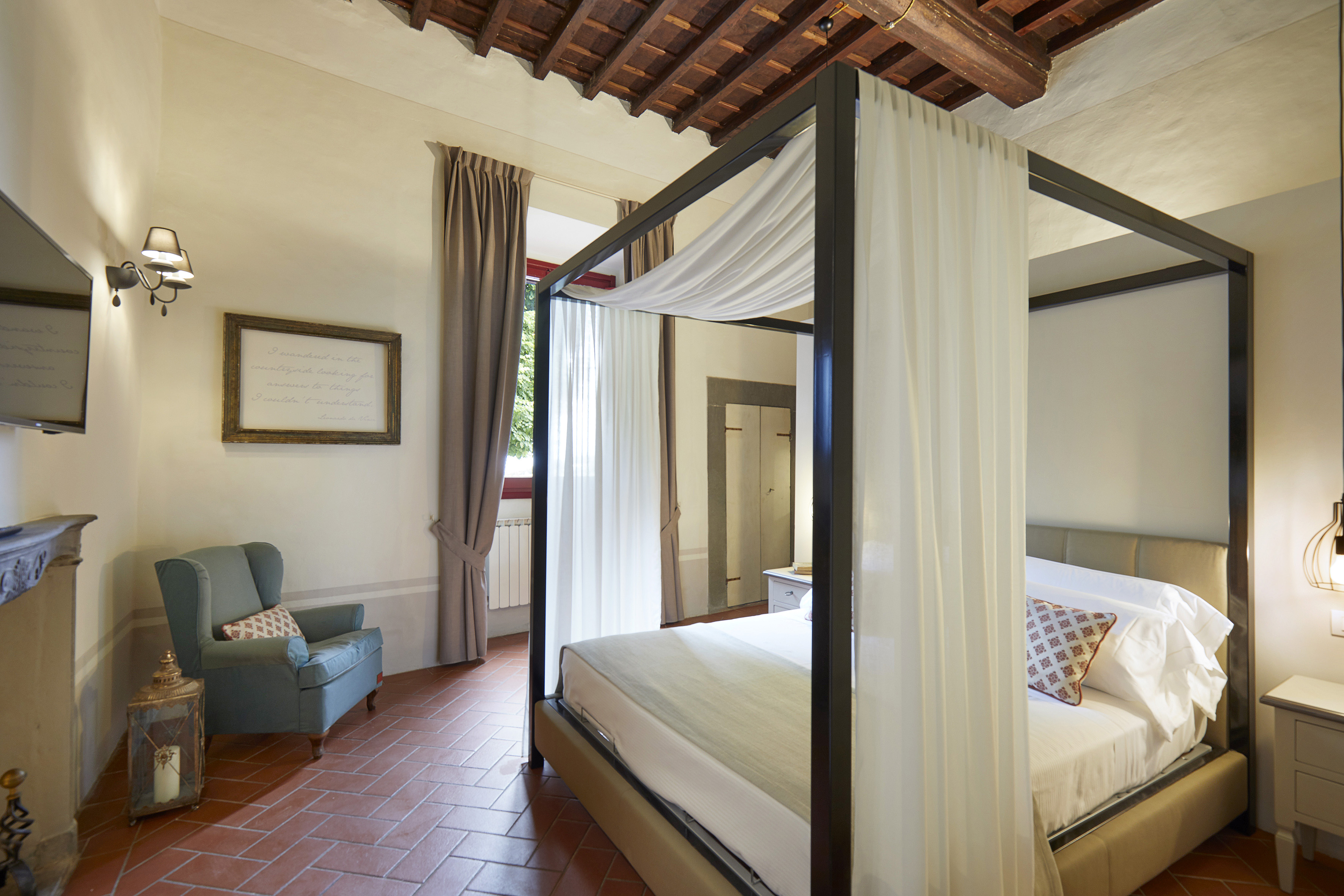 Rustic bedroom with four-poster bed, terracotta floor, and exposed wood beams.