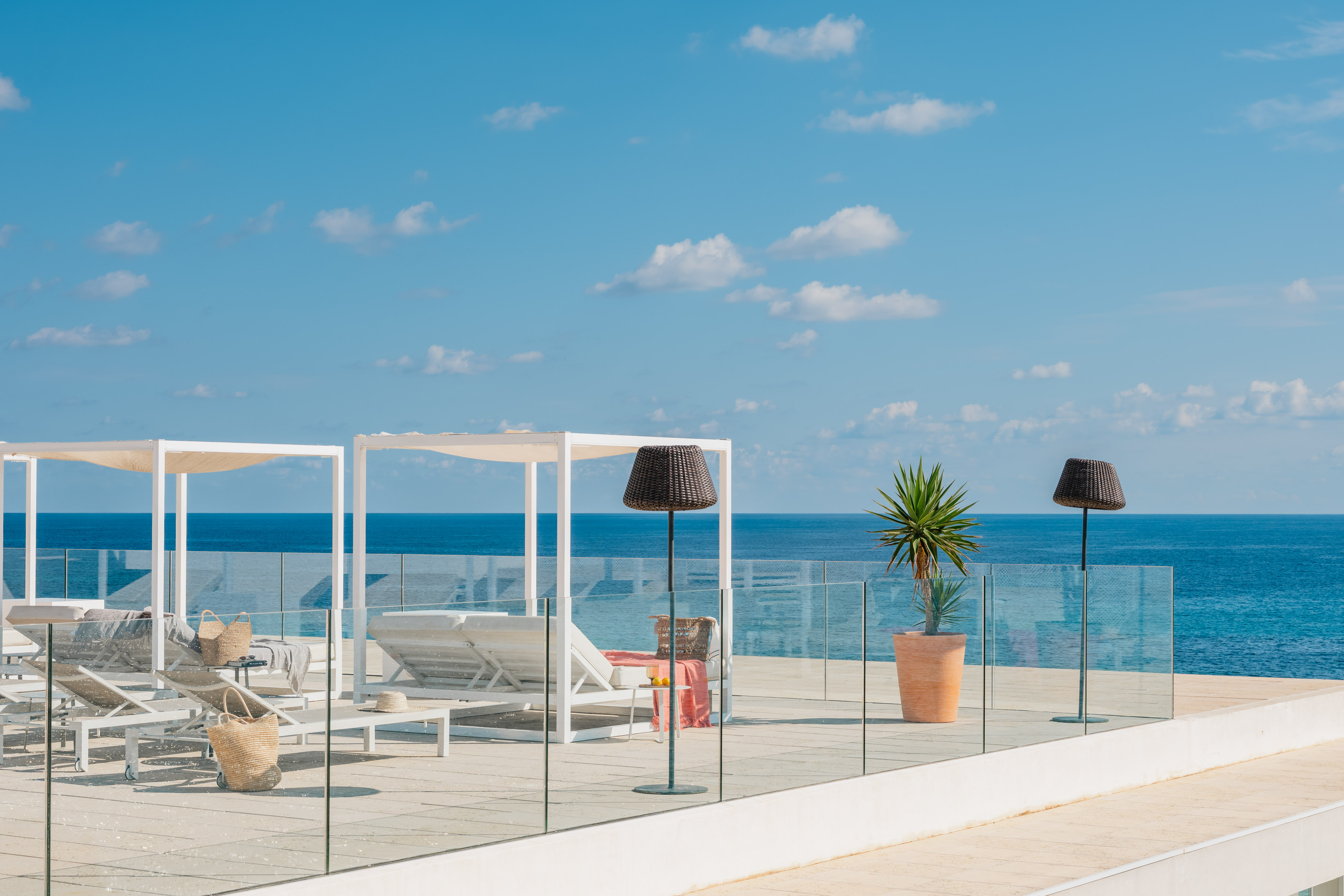 Sunny rooftop terrace, blue ocean view, modern lounge chairs, and pergolas.