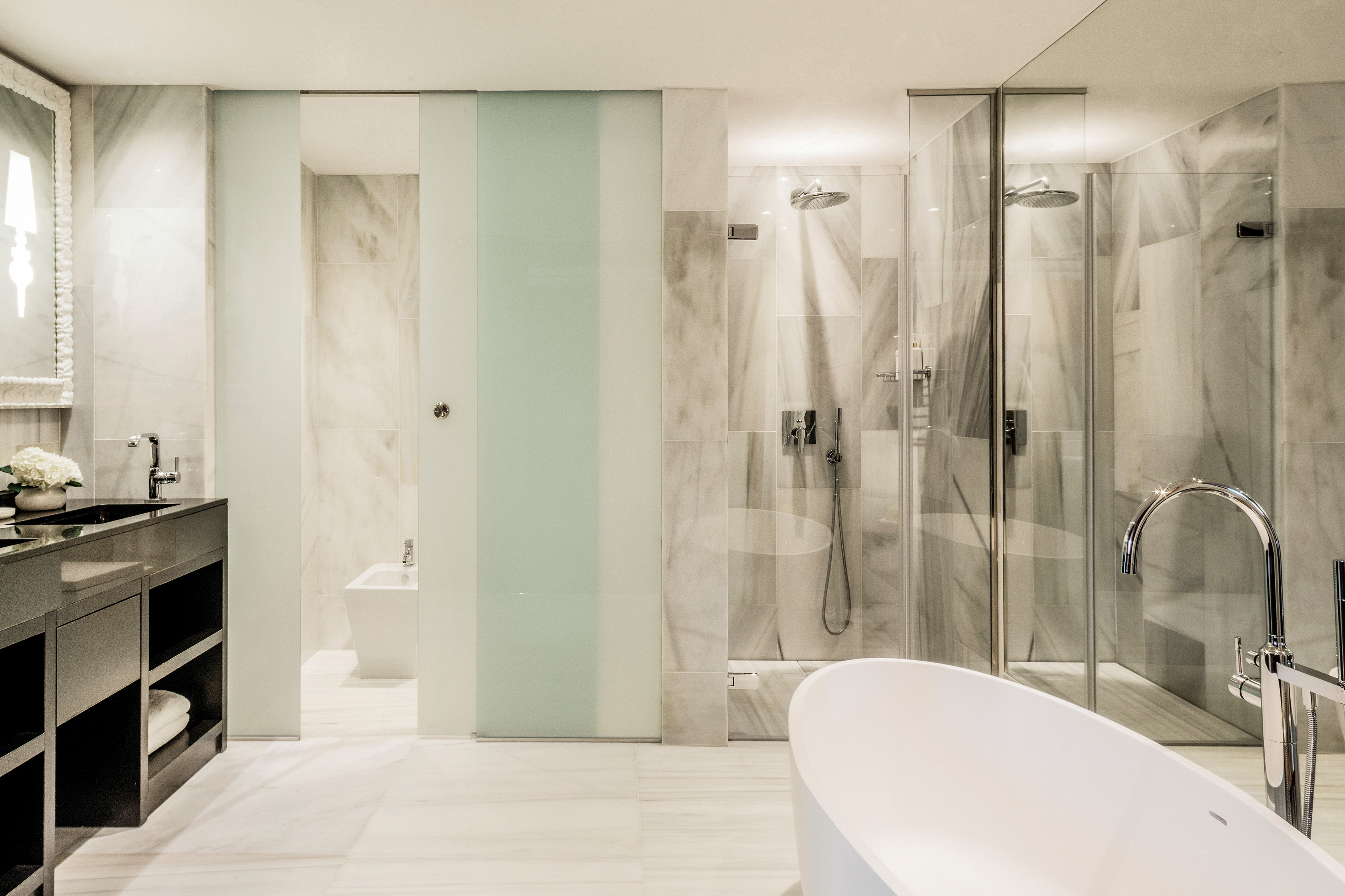 Luxury modern bathroom with marble, freestanding tub, and glass enclosed showers.
