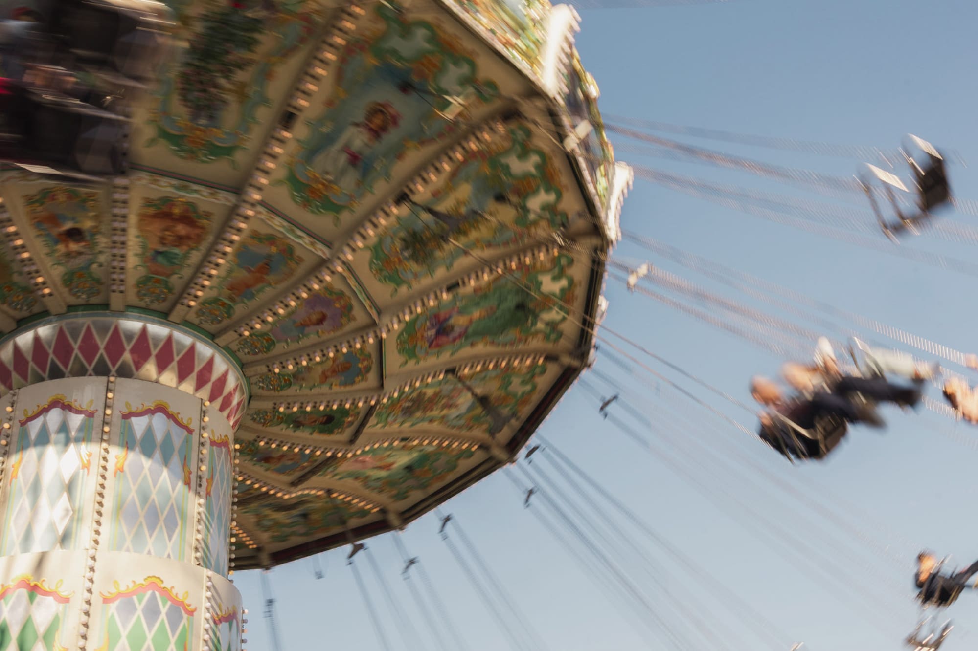 Motion-blurred swing ride with riders against blue sky and Christmas tree.