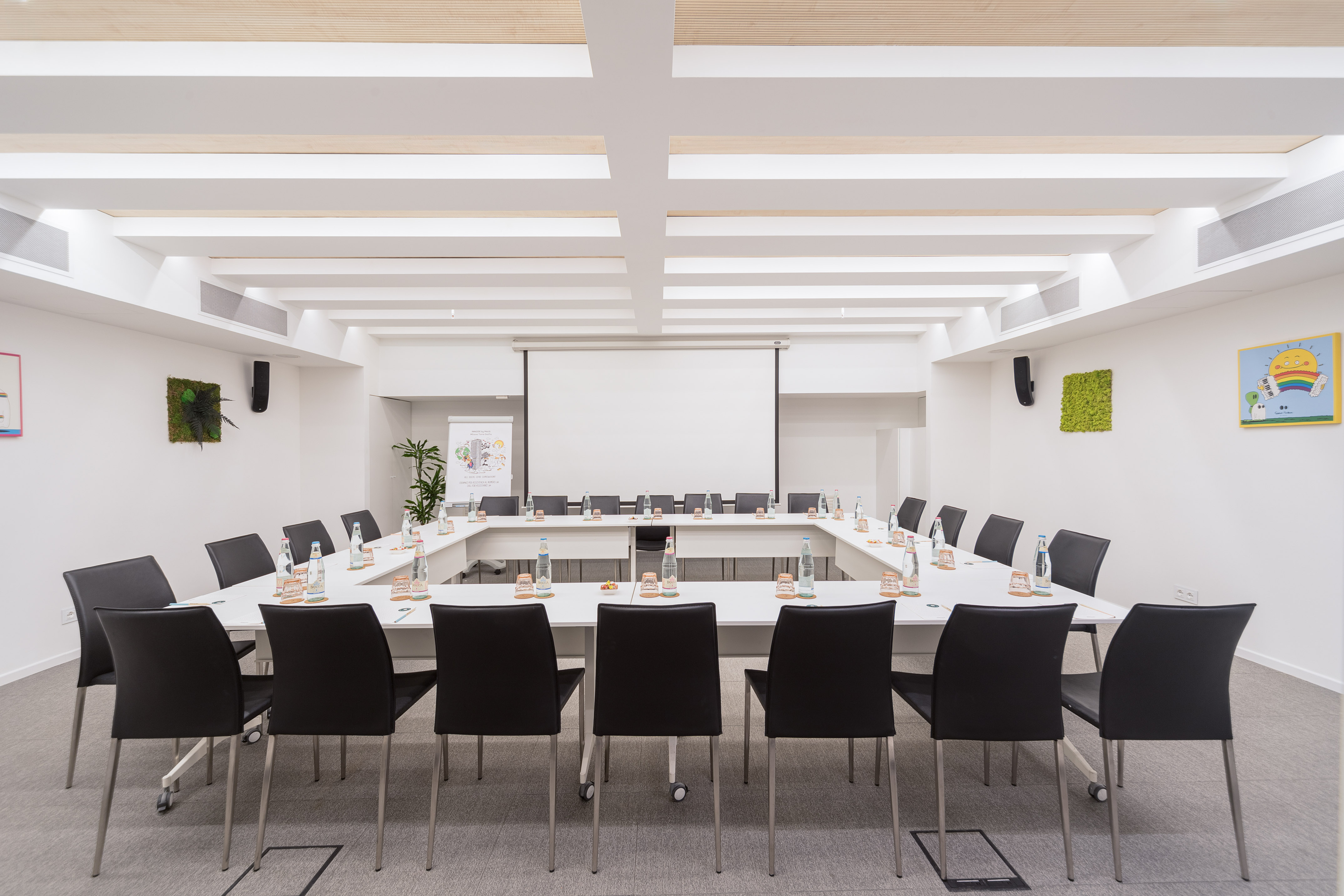 Modern U-shaped conference room with black chairs and projection screen.