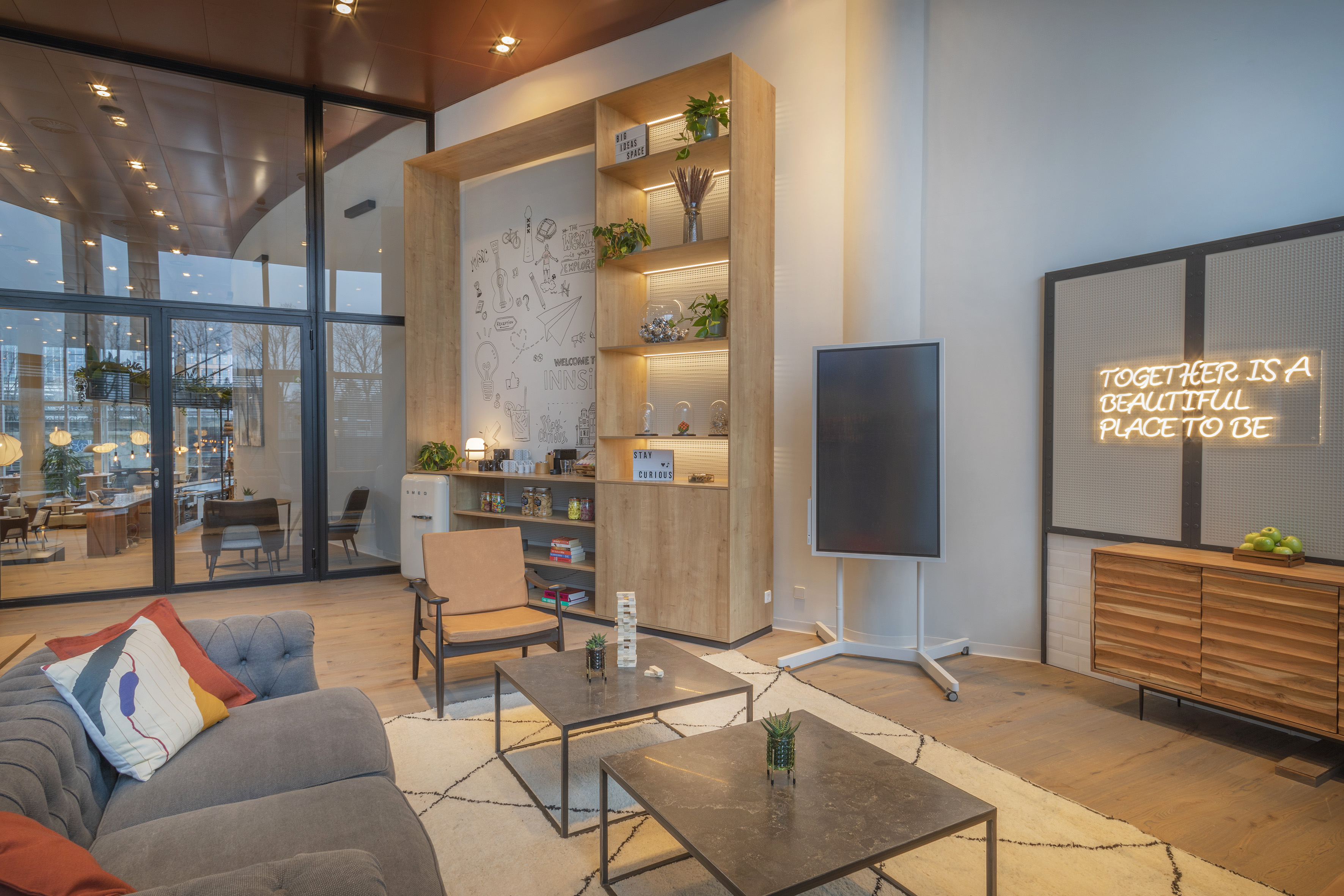 Modern lounge featuring sofa, wooden shelves, large windows, and a neon sign.