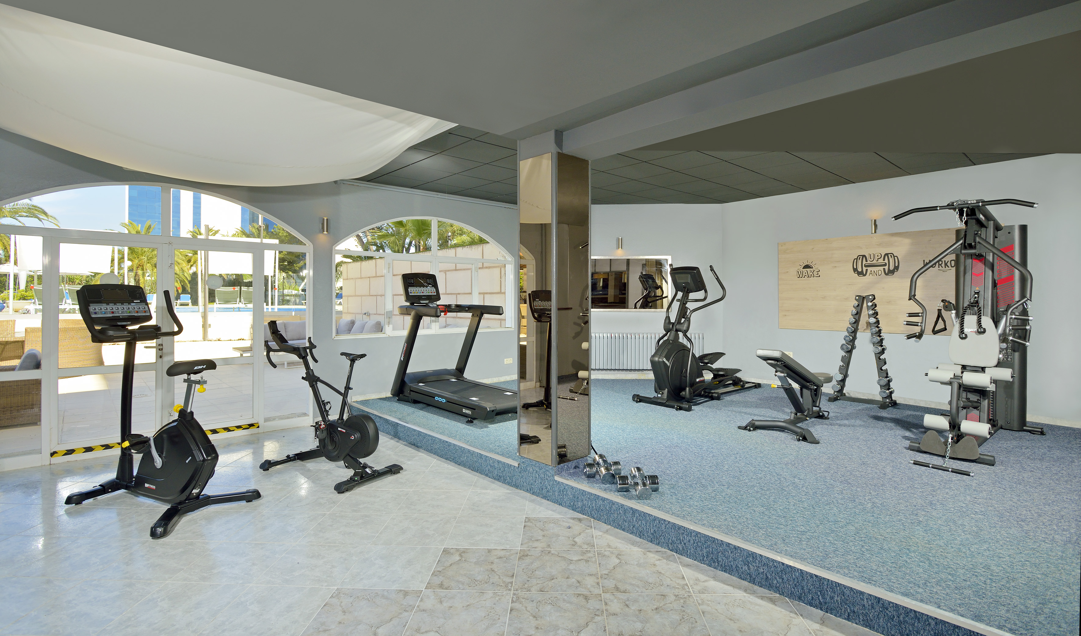 Spacious hotel fitness center with treadmills, bikes, weights, and pool view.
