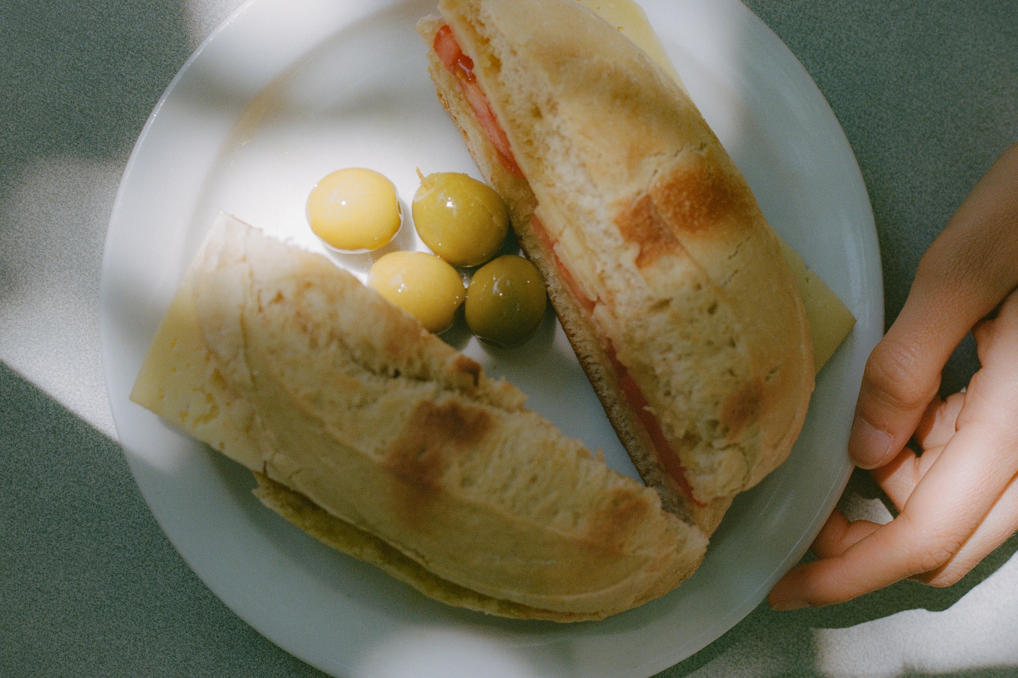 Desayuno español: bocadillo y aceitunas en plato blanco con luz solar.