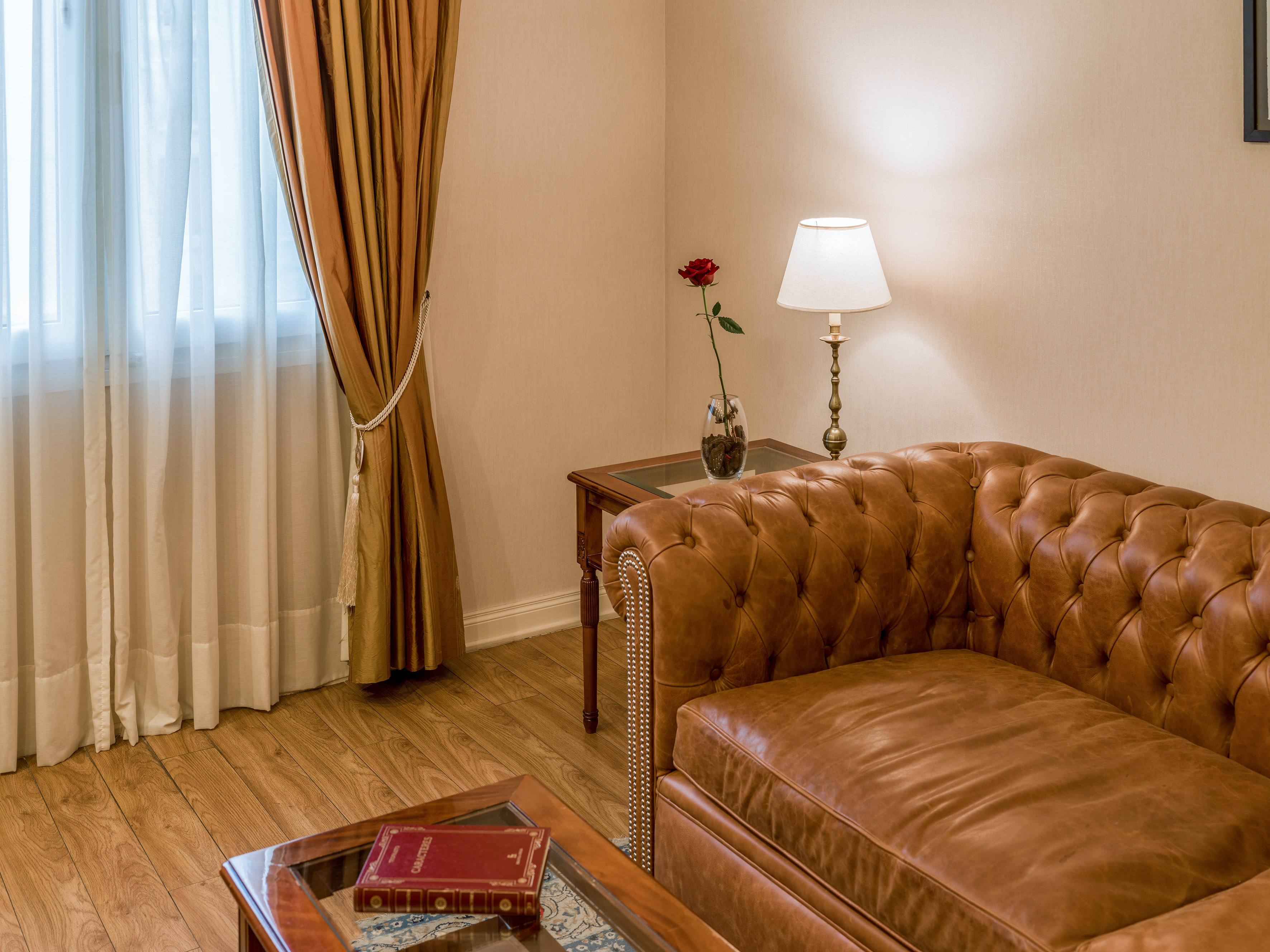 Tufted brown leather Chesterfield sofa, lamp, rose, window in a hotel room.