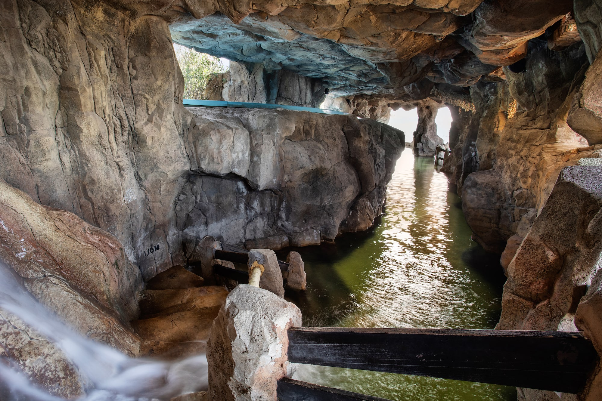 Grotto interior with water channel, waterfall, light, and stone walls.