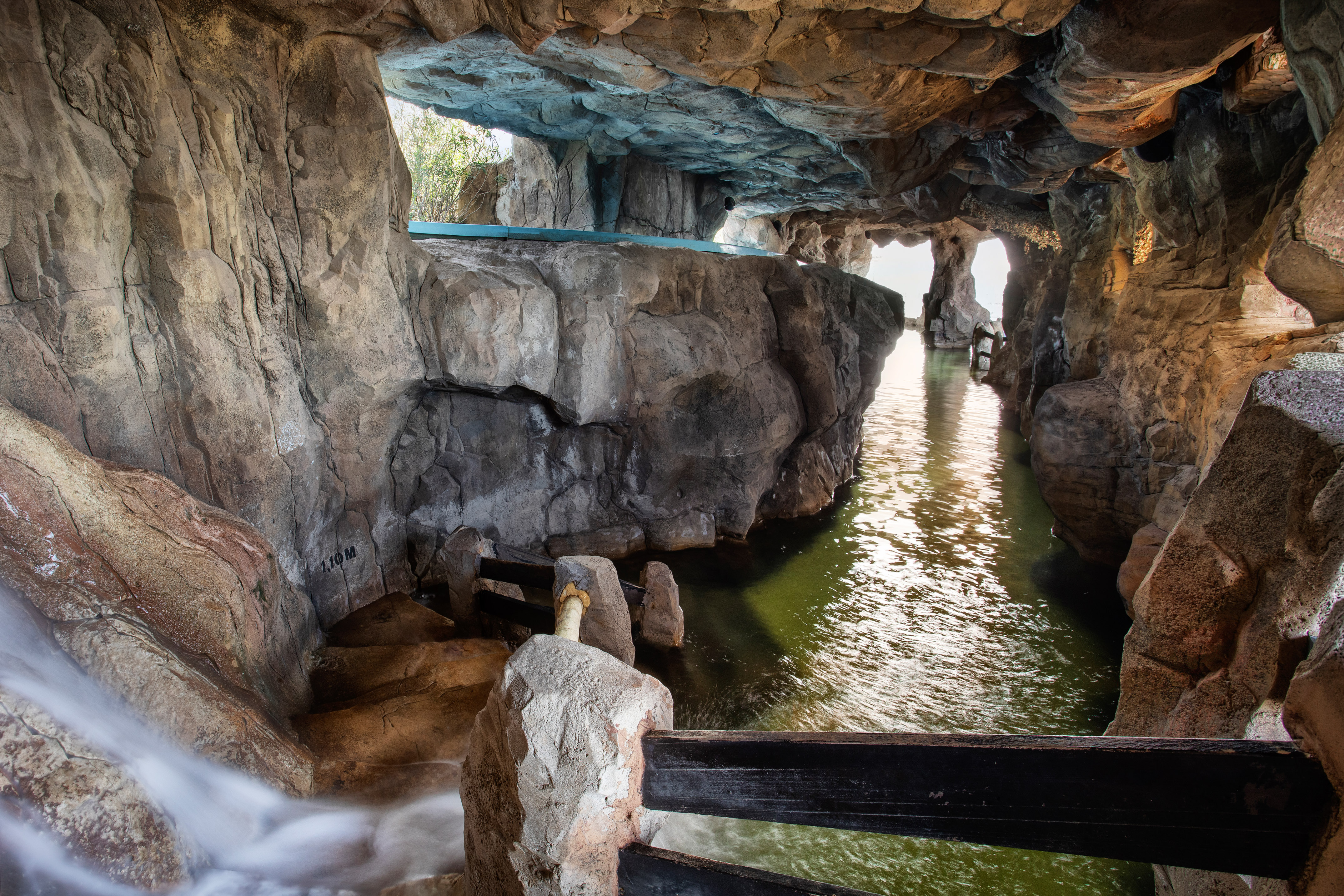 Grotto interior with water channel, waterfall, light, and stone walls.