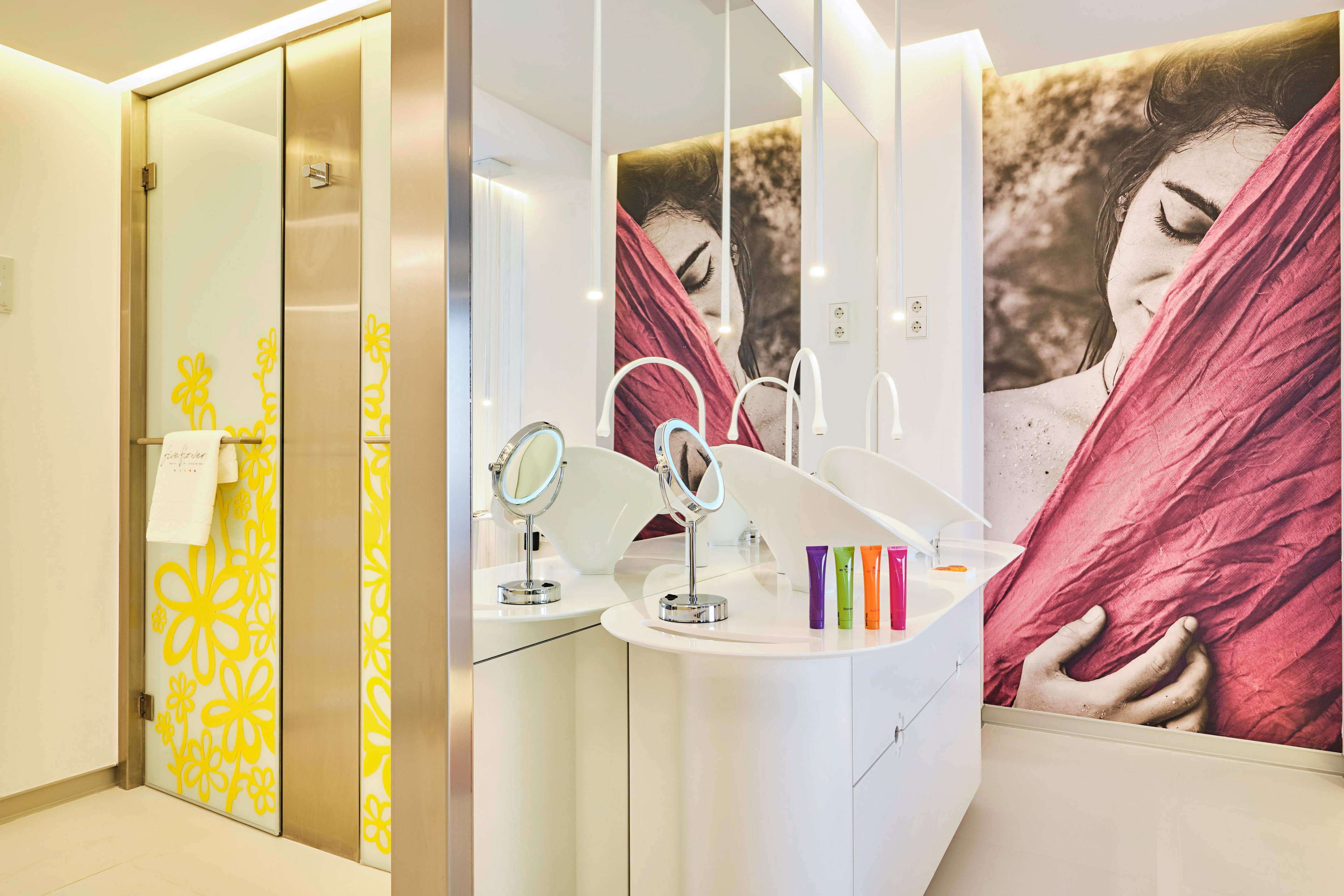 Bright bathroom with double vanity, woman mural, and yellow floral glass door.