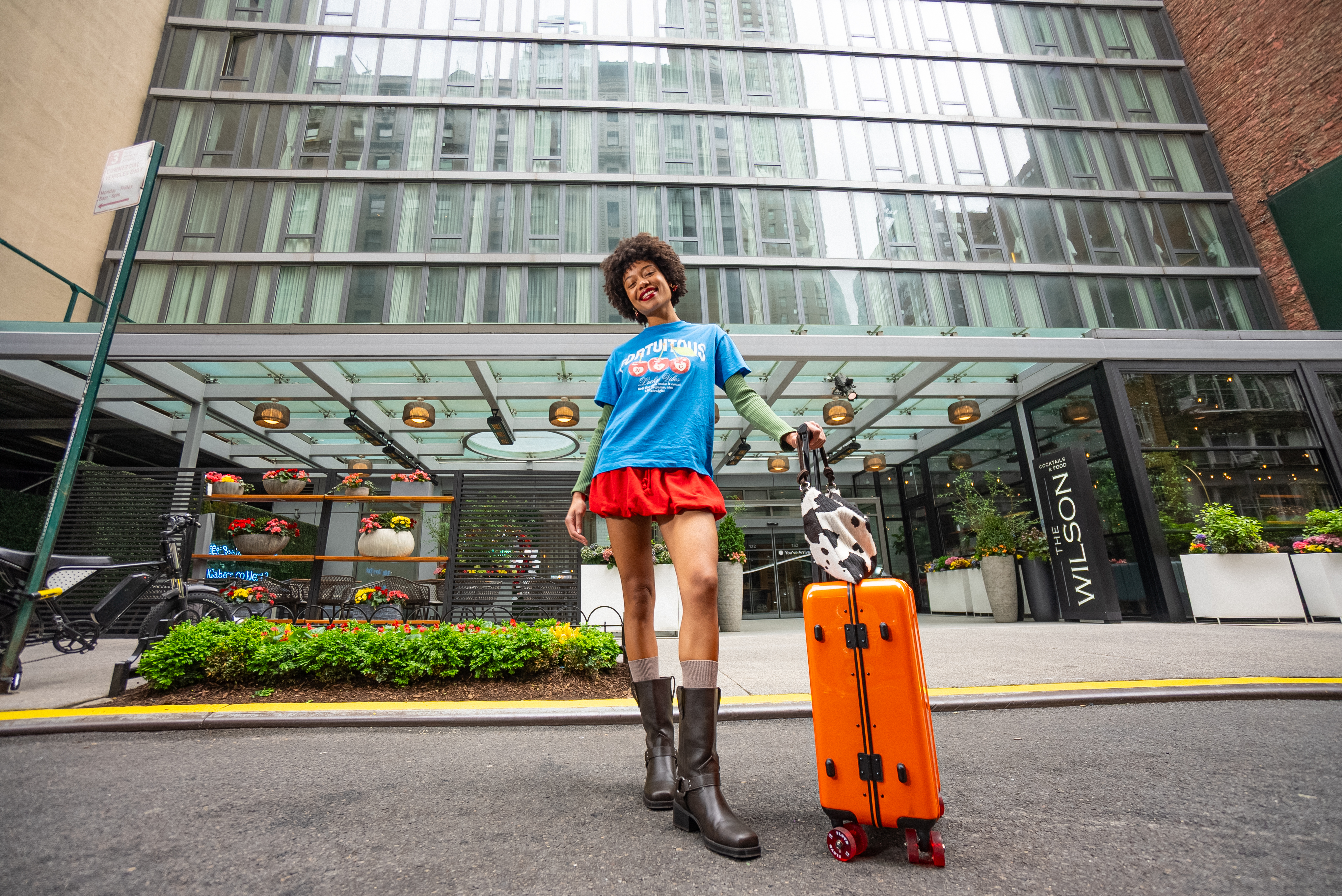 Woman traveler with orange suitcase outside The Wilson Hotel.
