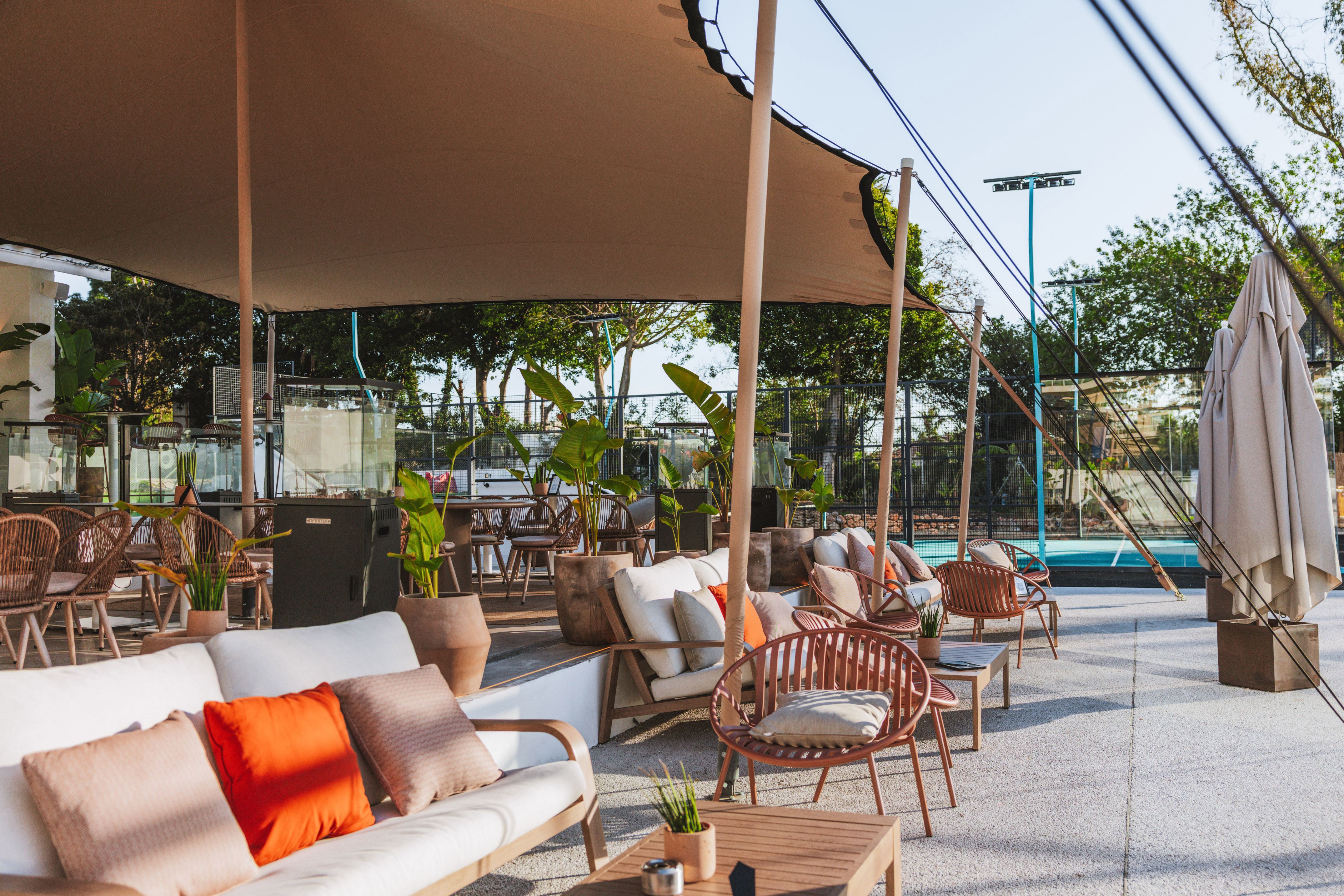 Al fresco patio with modern seating, large canopy, and blue padel court.