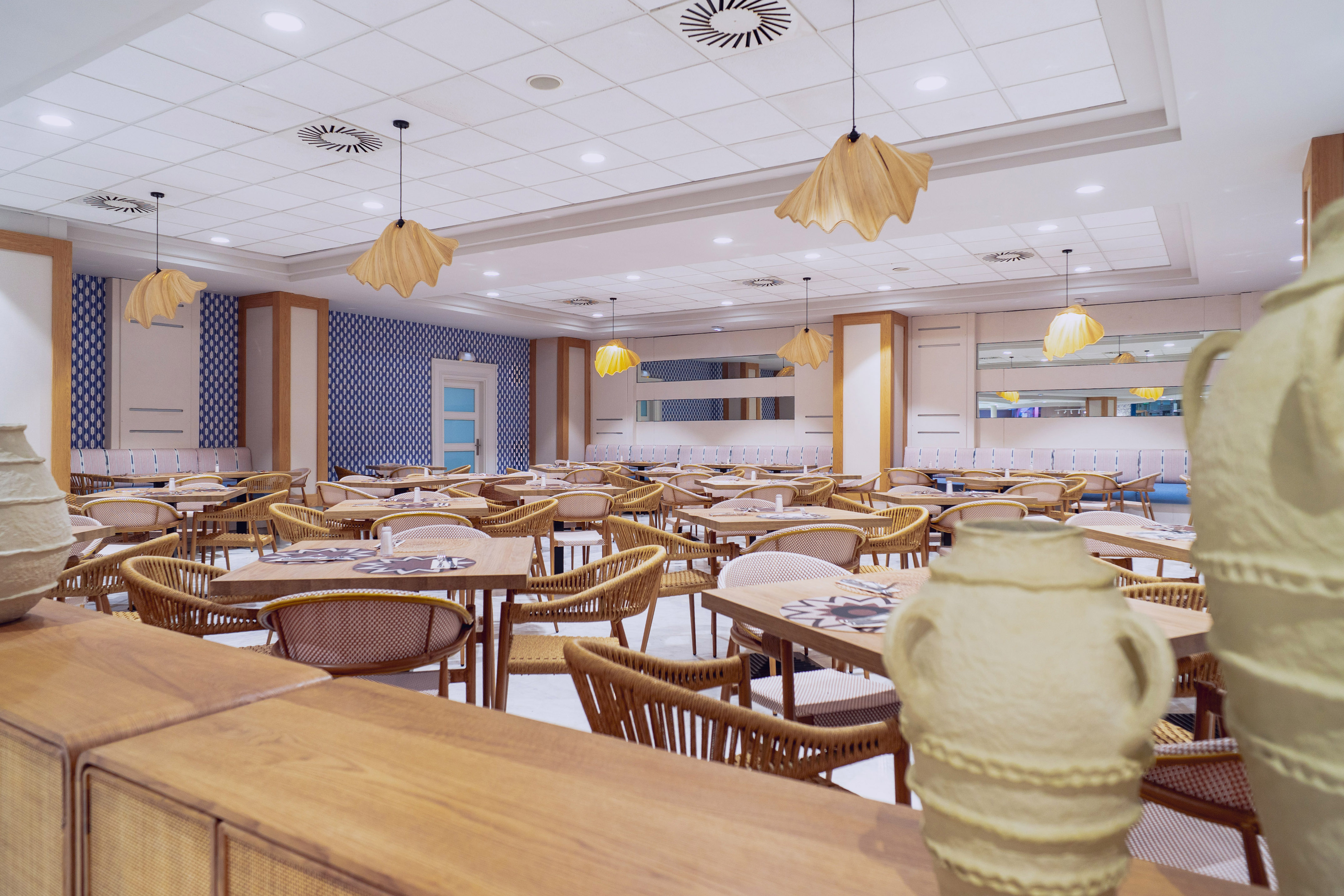 Spacious hotel restaurant with blue patterned walls, wooden tables, and wicker chairs.