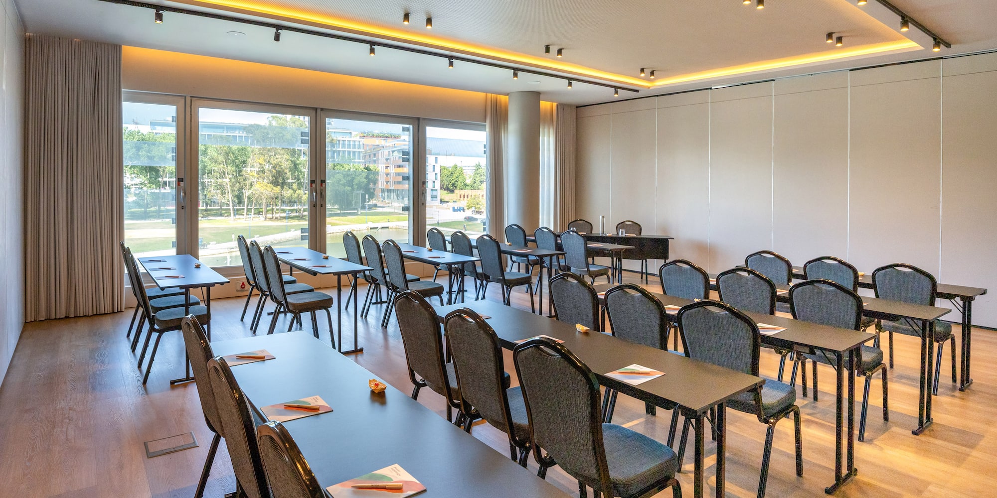 Modern conference room with classroom setup, large windows, city view, and wood floor.