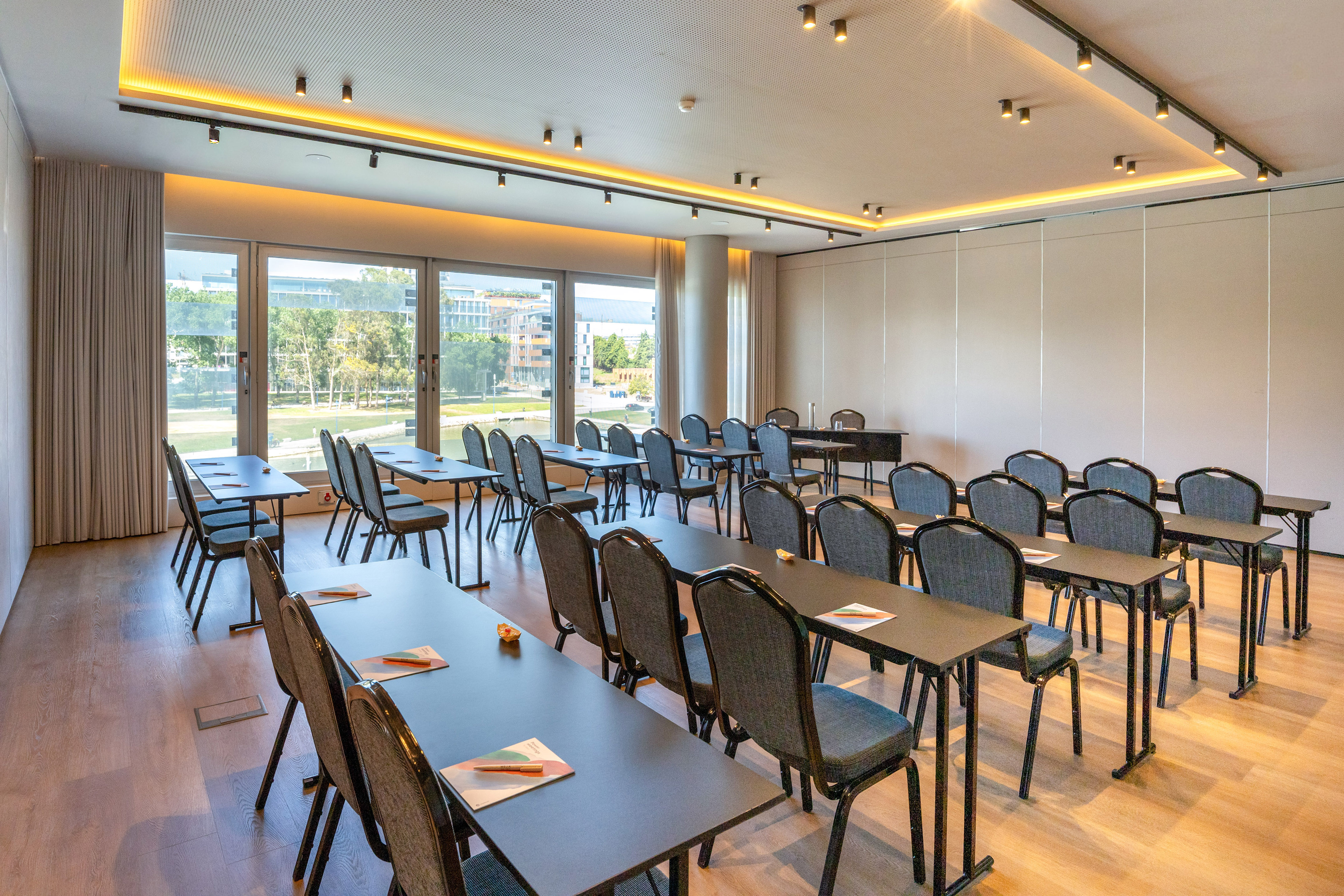 Modern conference room with classroom setup, large windows, city view, and wood floor.