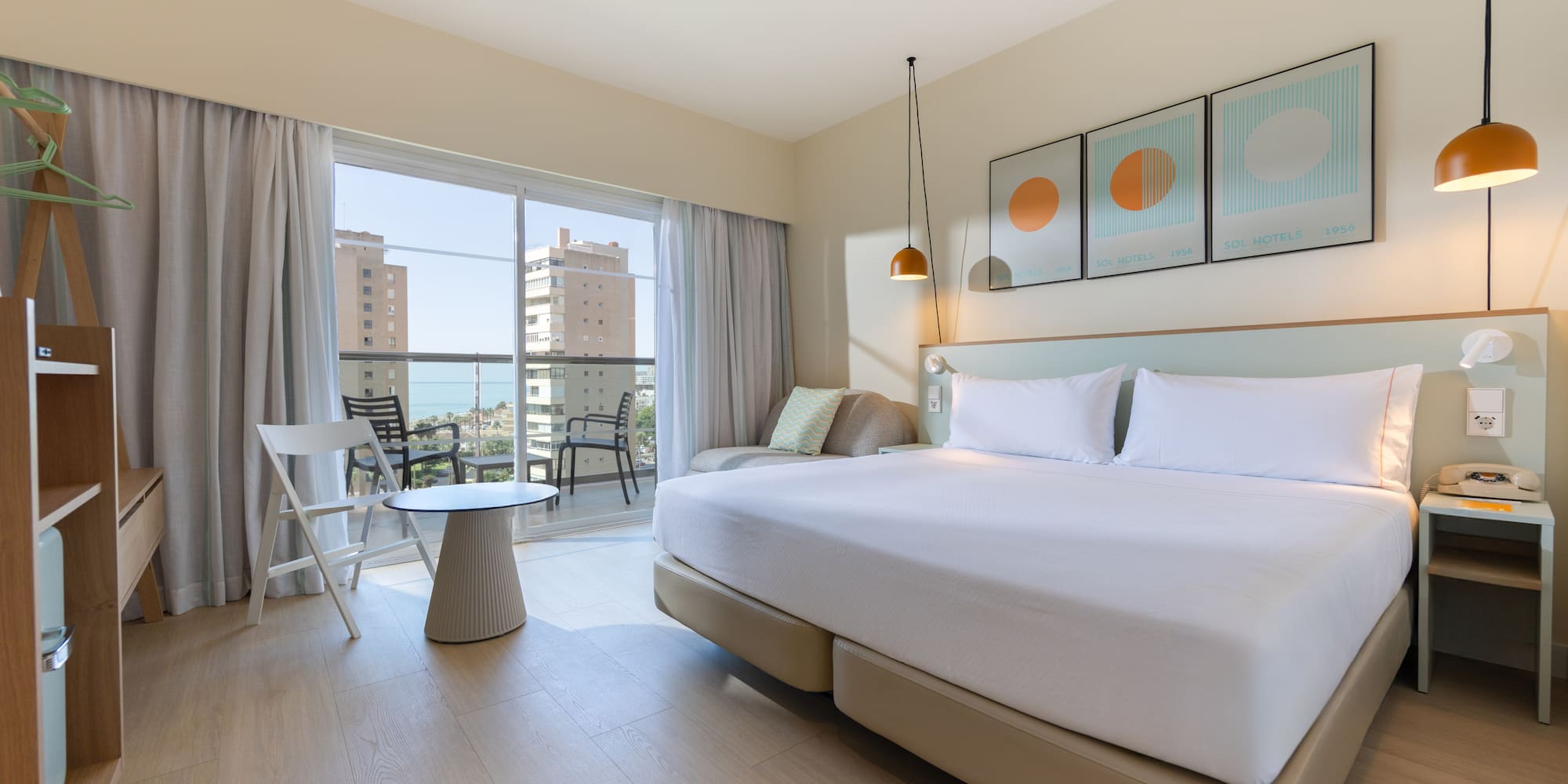 Modern hotel room with large bed, balcony, and sea view.