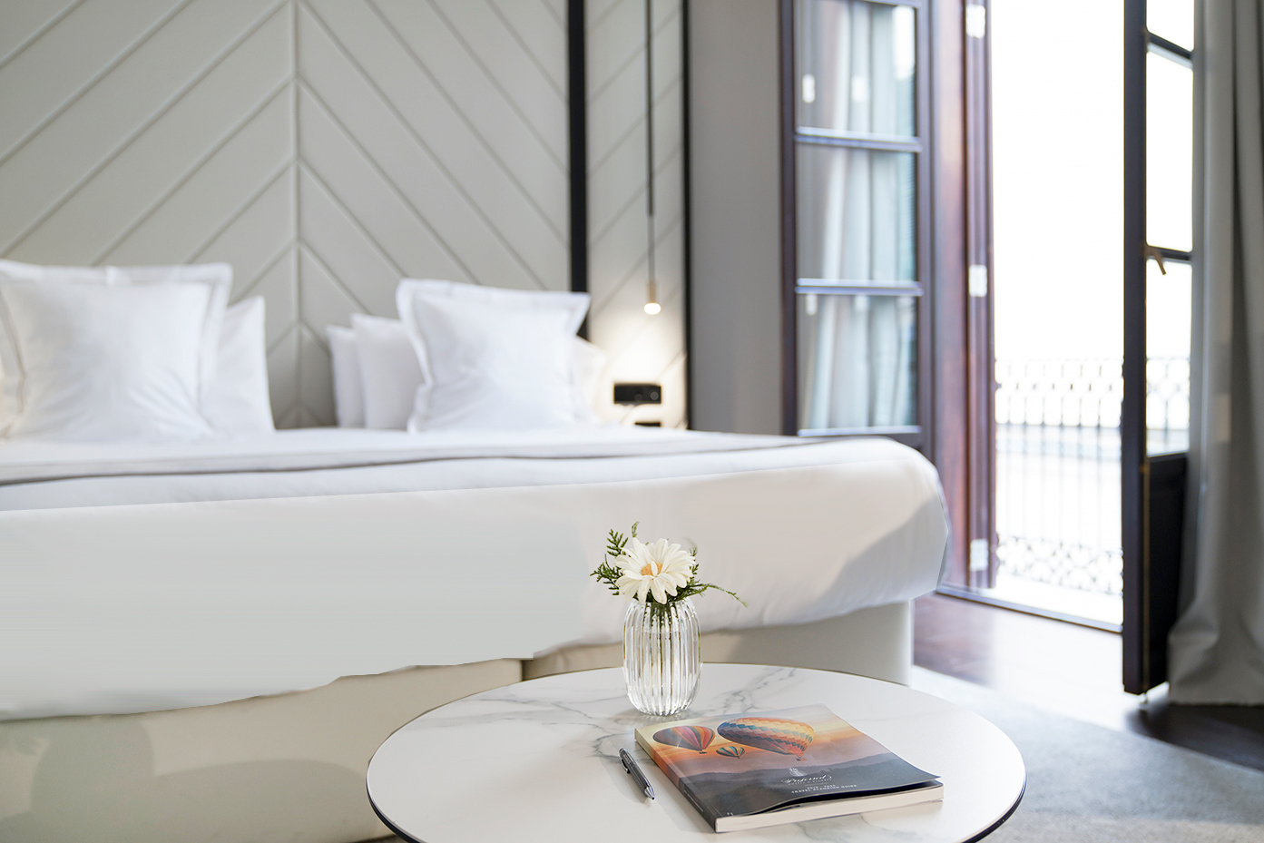 Luxury hotel bedroom with white bed, table with flowers, and balcony.