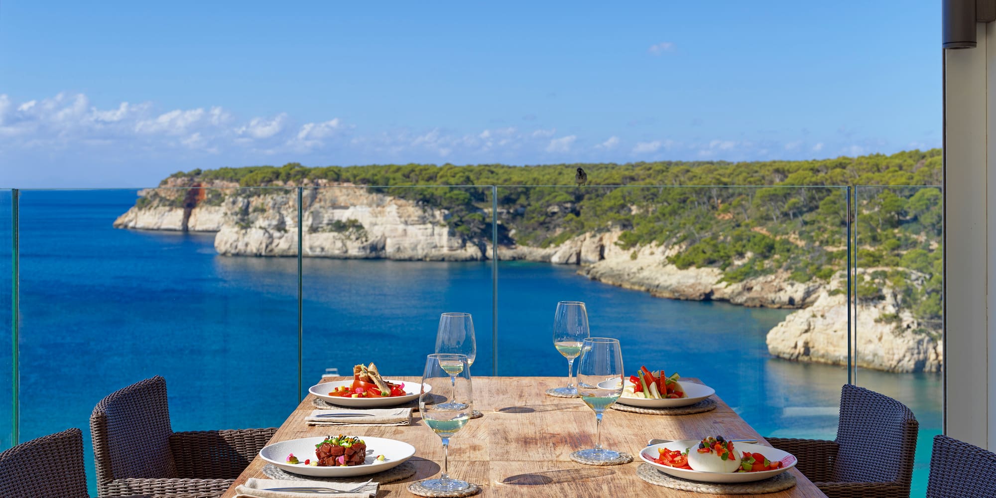 a table with plates of food and wine glasses on it overlooking a body of water