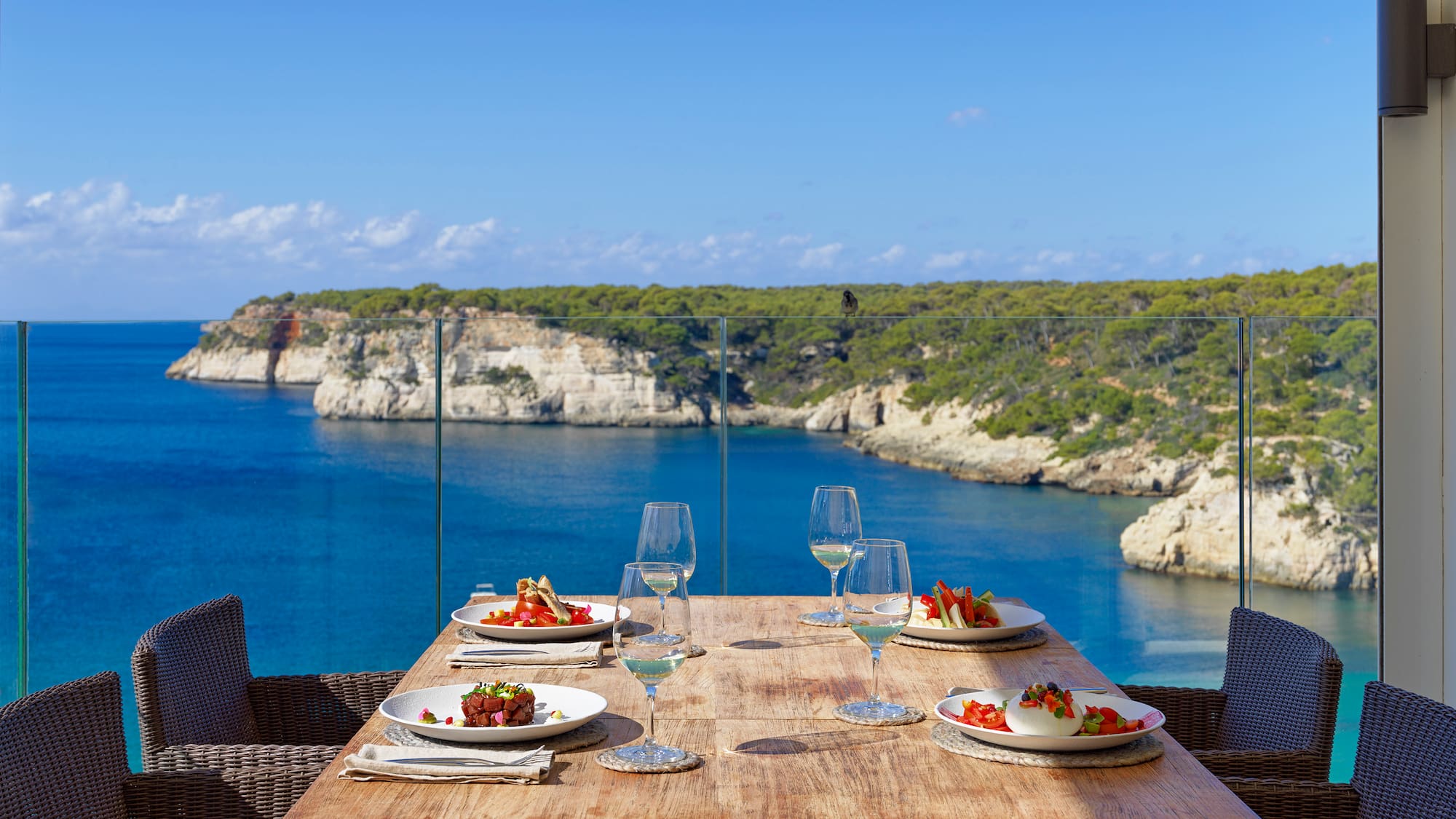a table with plates of food and wine glasses on it overlooking a body of water