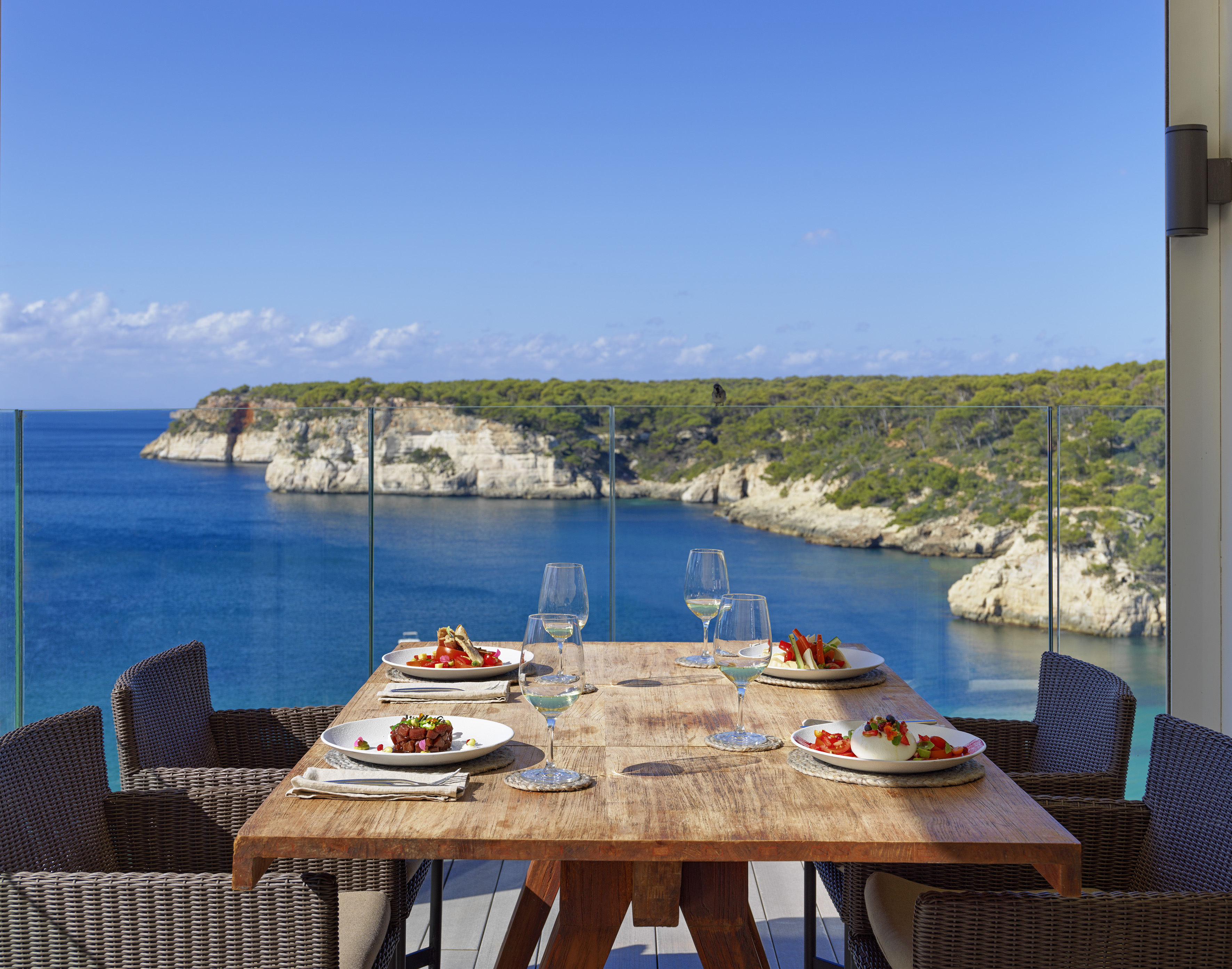 a table with plates of food and wine glasses on it overlooking a body of water