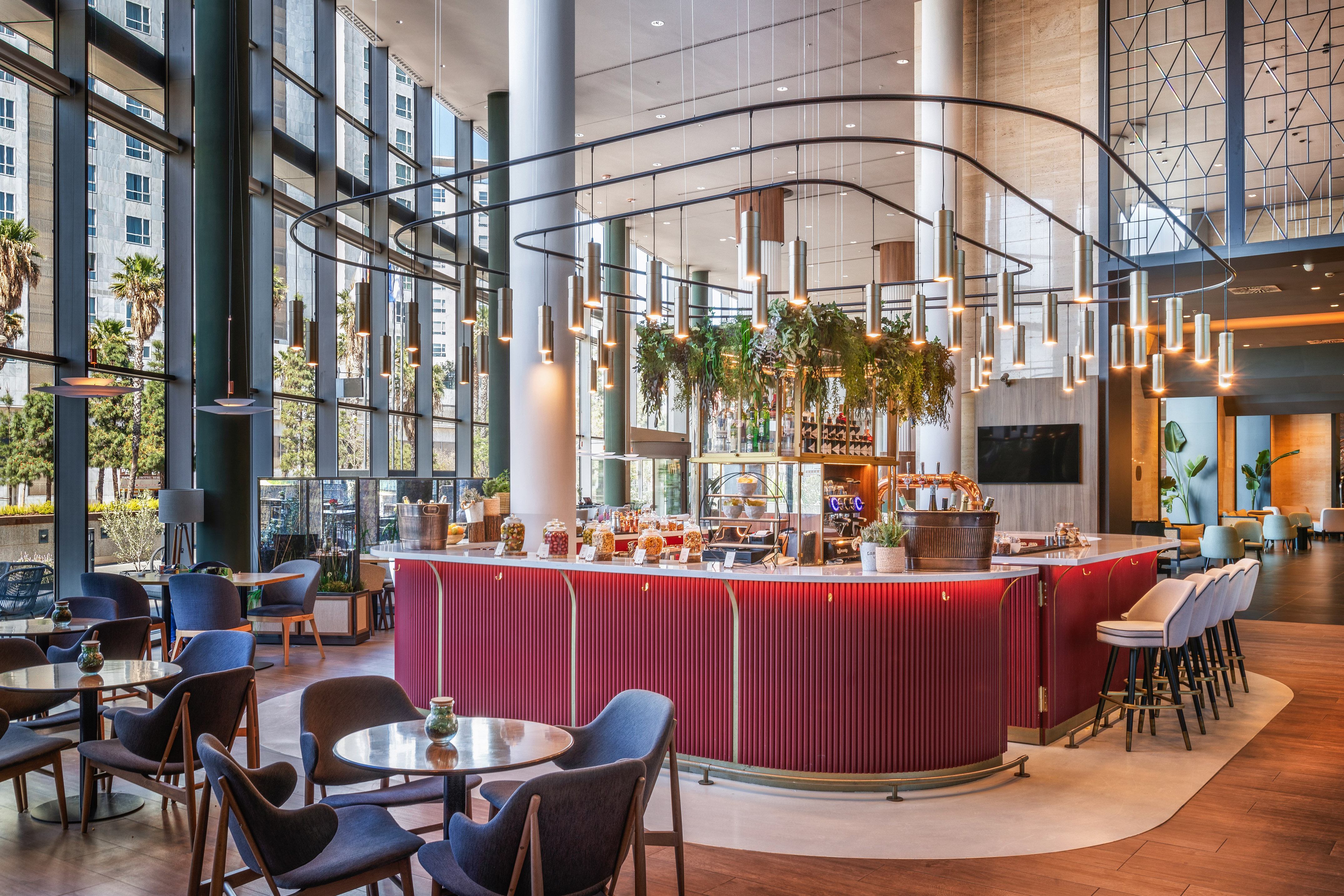 Modern hotel lobby bar with red counter, stylish seating, city view.