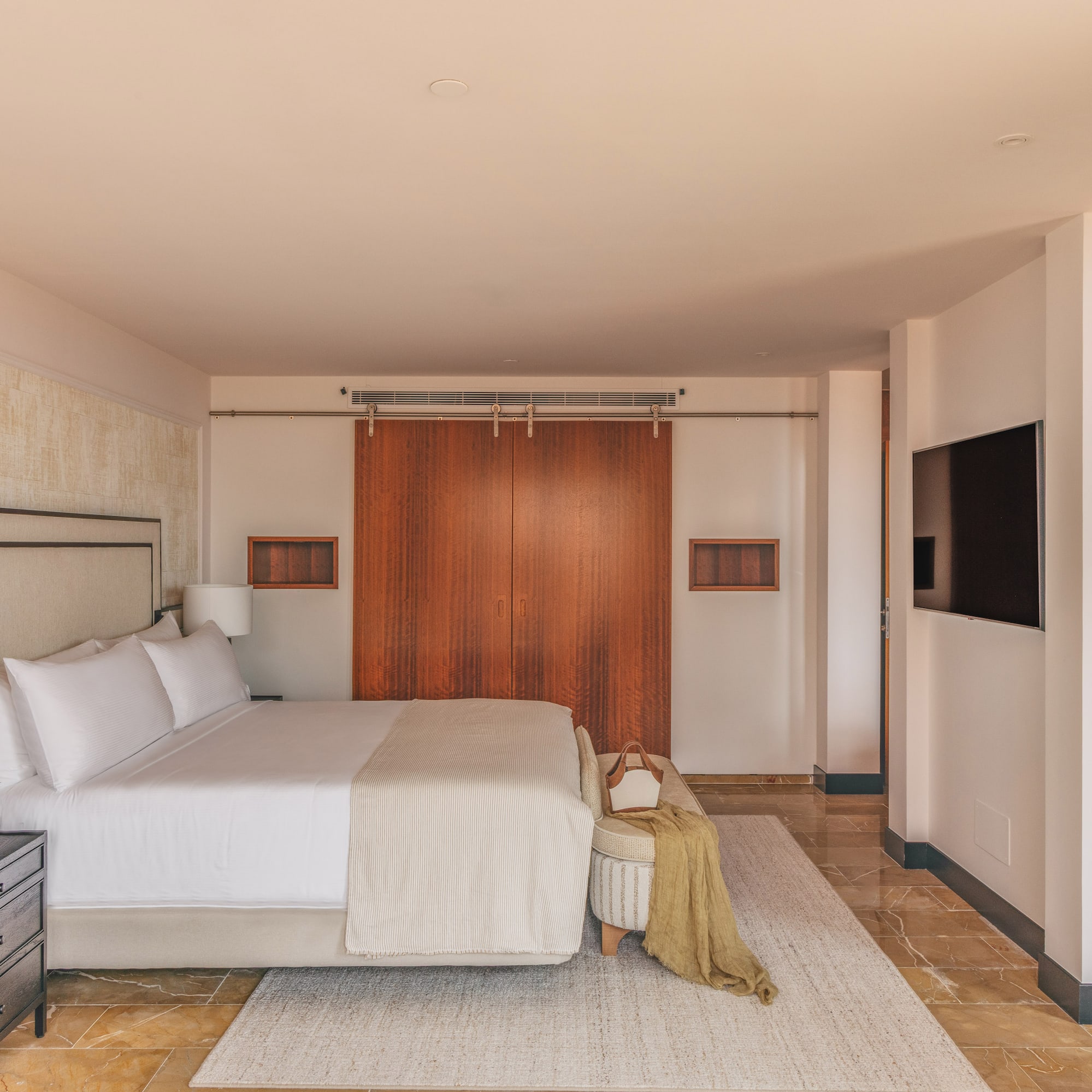 Luxurious modern bedroom with king bed, wooden doors, wall-mounted TV, and marble floor.