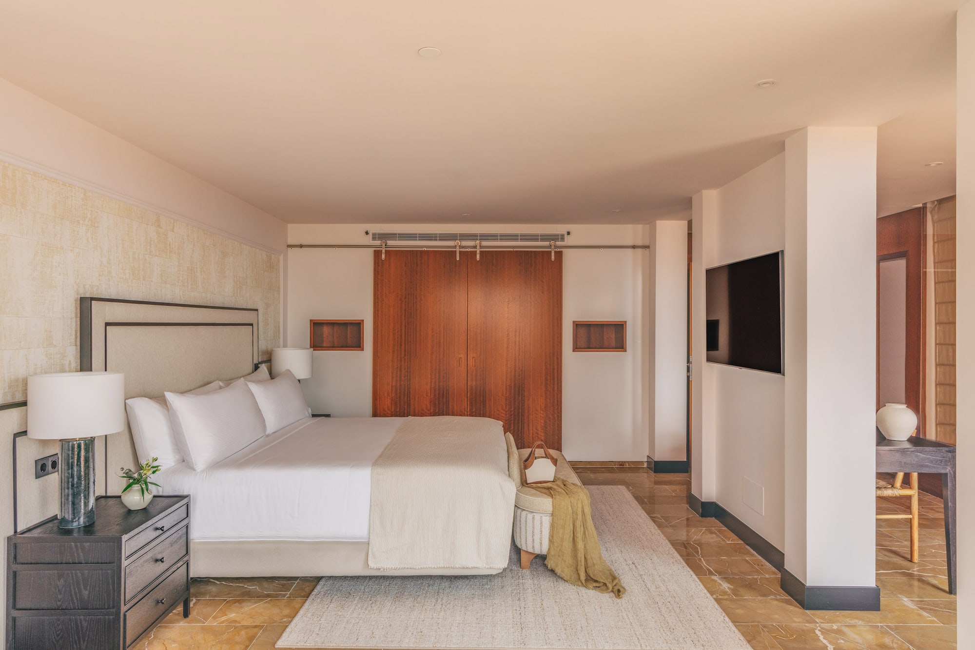 Luxurious modern bedroom with king bed, wooden doors, wall-mounted TV, and marble floor.