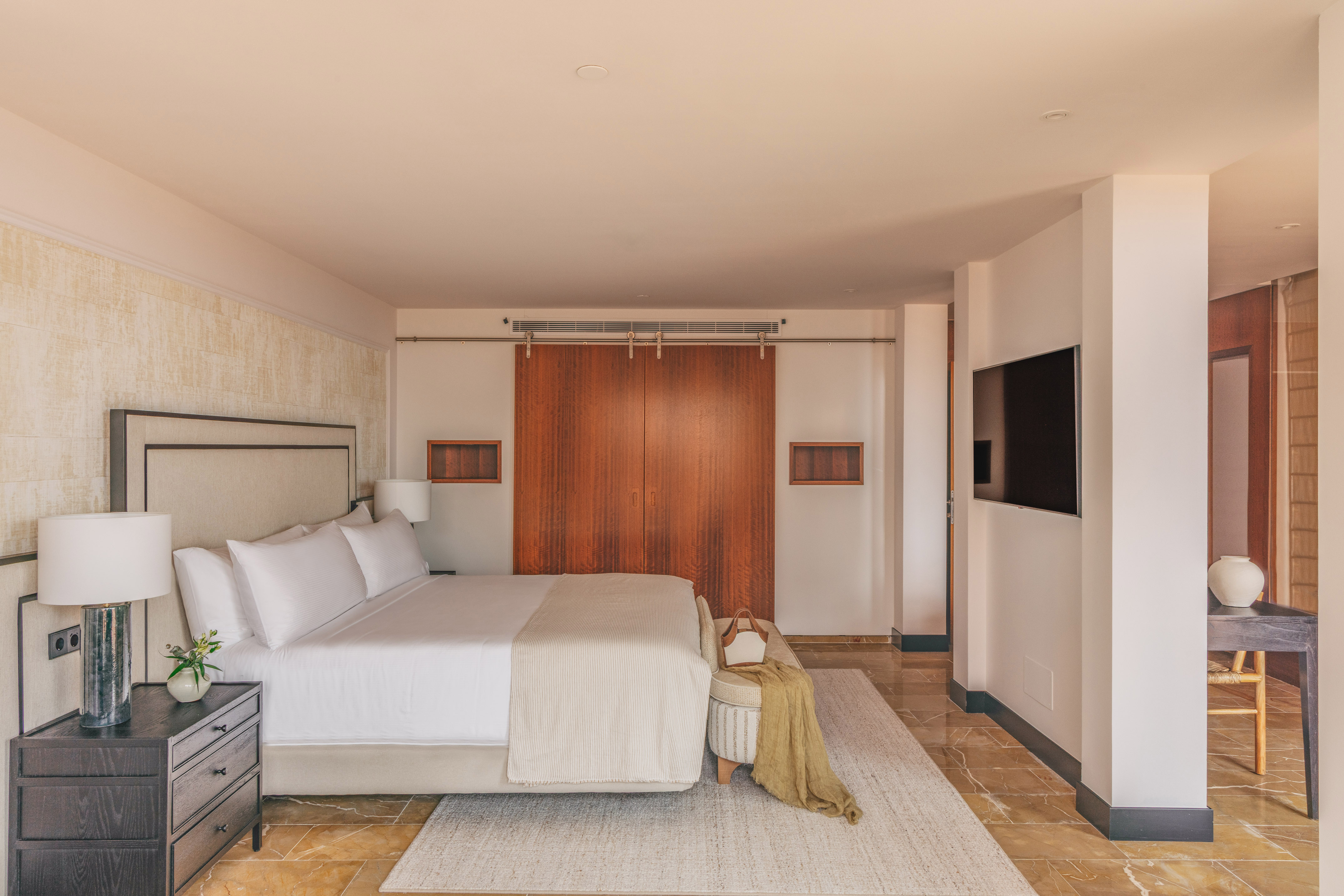 Luxurious modern bedroom with king bed, wooden doors, wall-mounted TV, and marble floor.