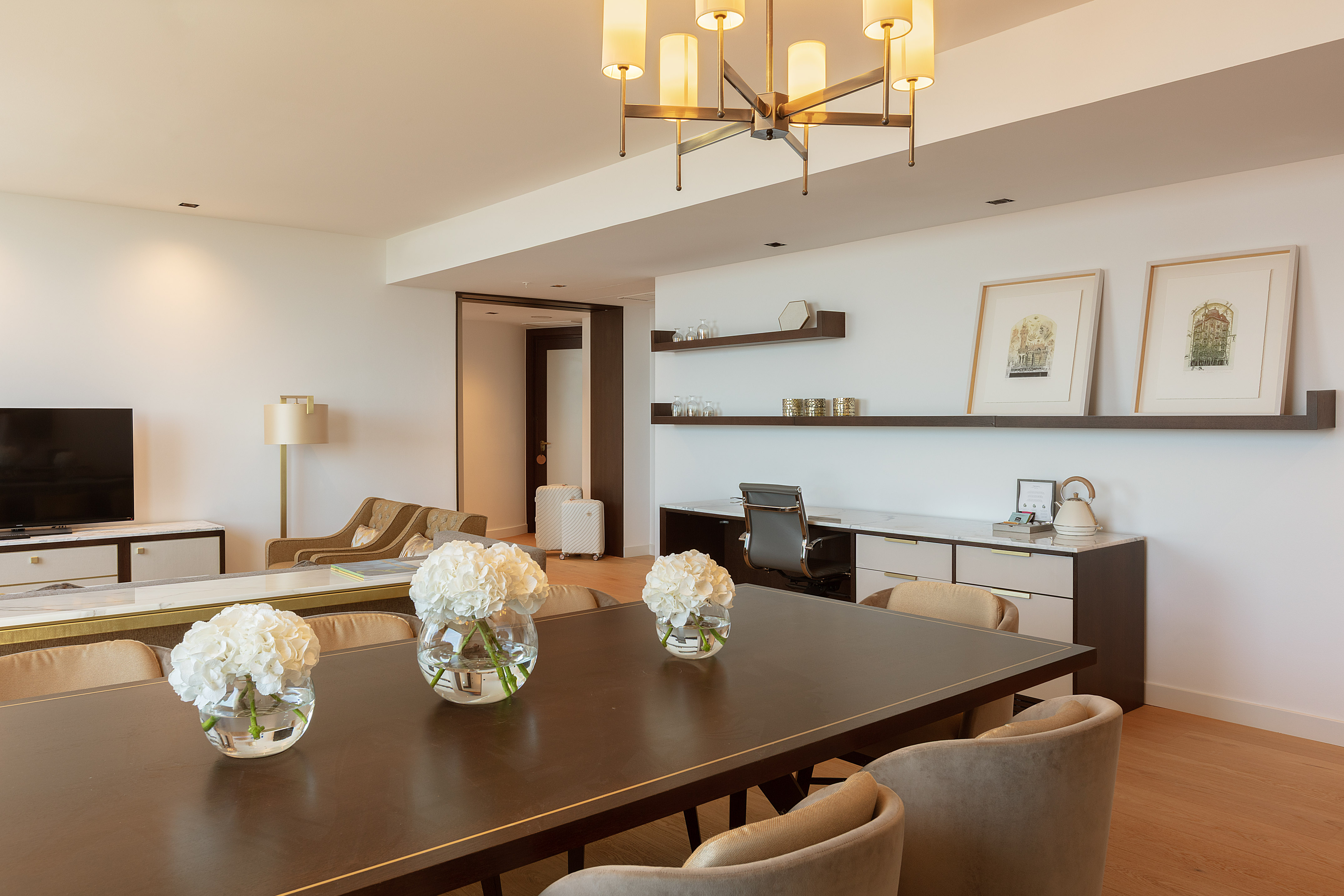Bright modern hotel suite with dining table, living area, and office desk.