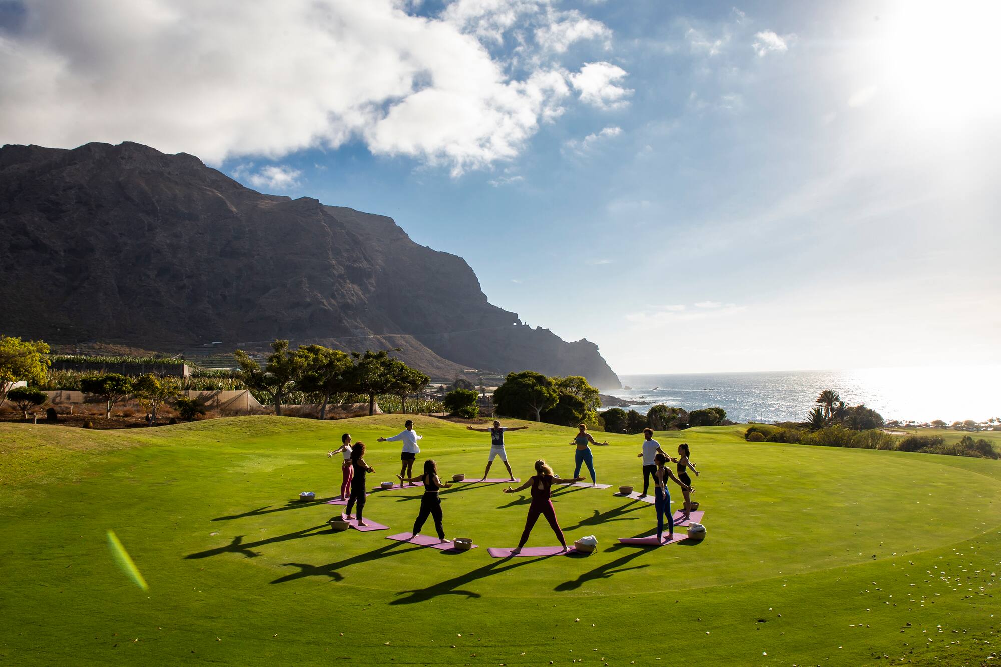 Outdoor yoga class on green field overlooking ocean and mountains.