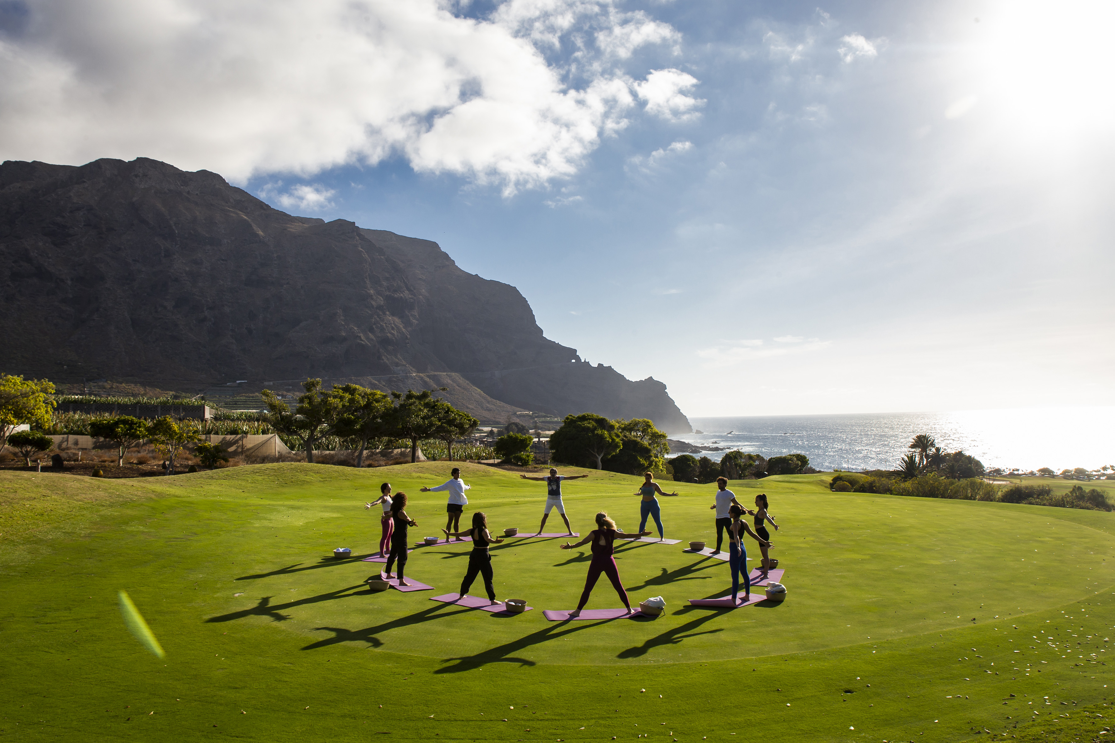 Outdoor yoga class on green field overlooking ocean and mountains.