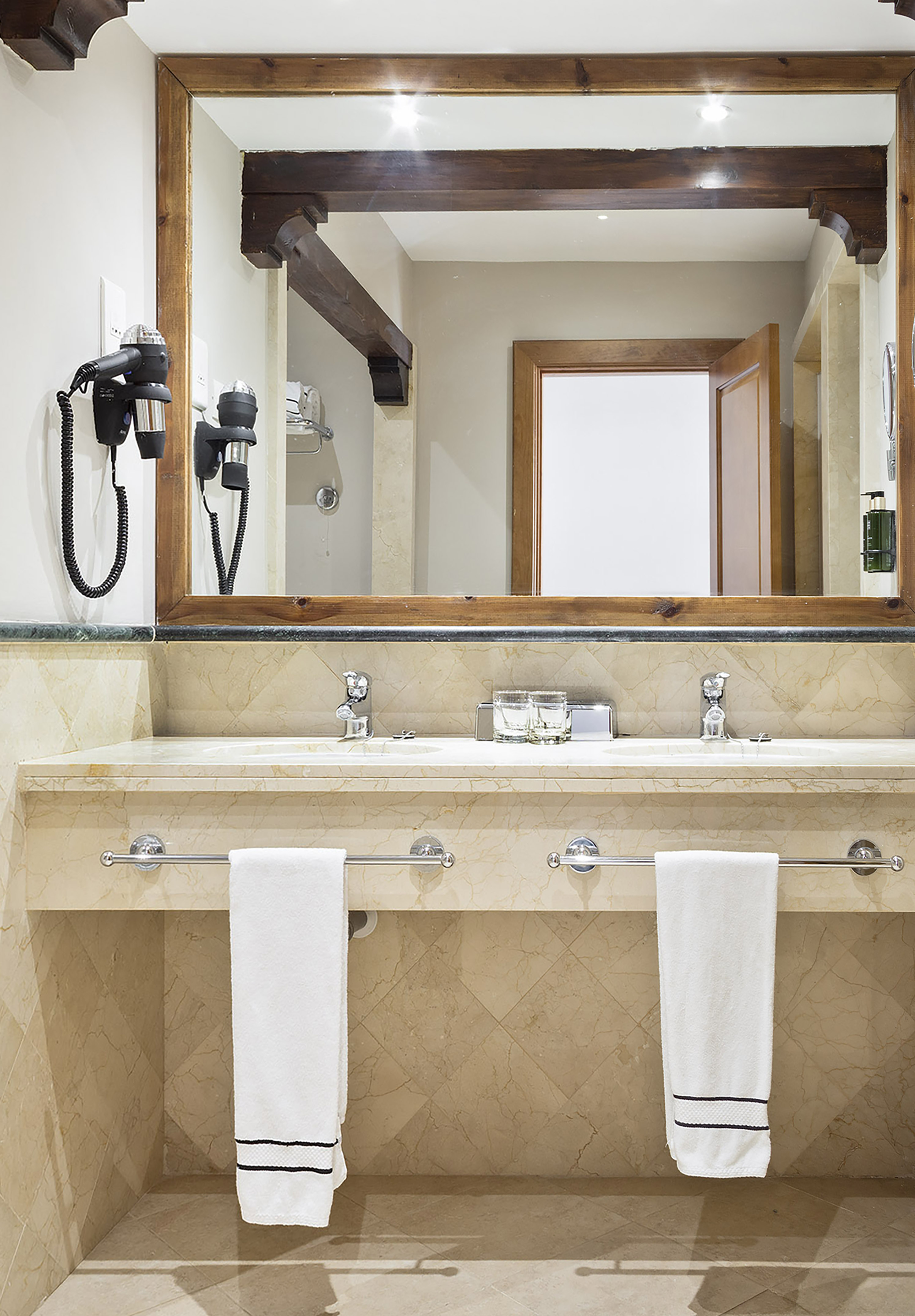 Hotel bathroom with double marble vanity, rustic wooden mirror, and hairdryer.