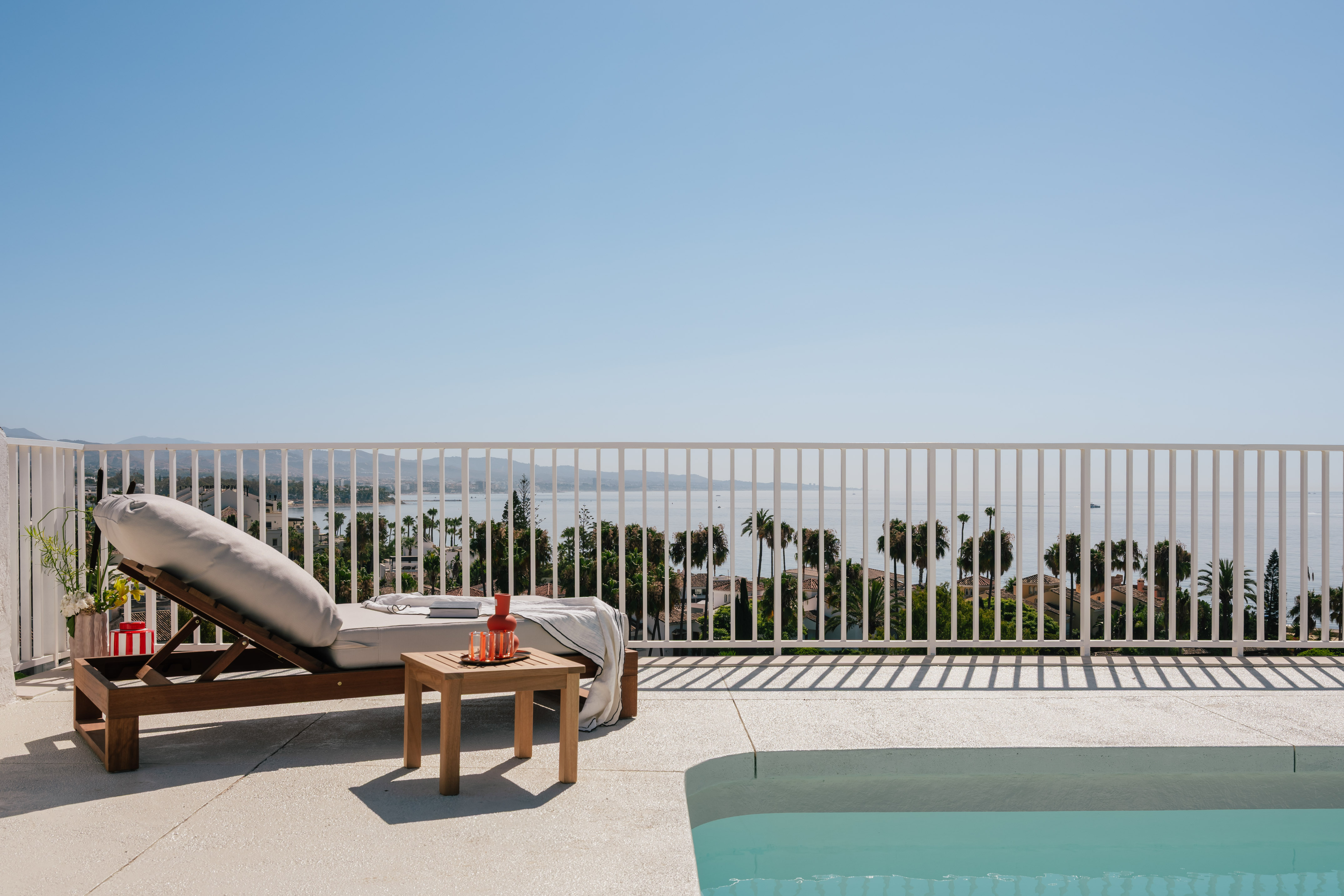 Lounge chair and pool on a patio with a stunning sea view.