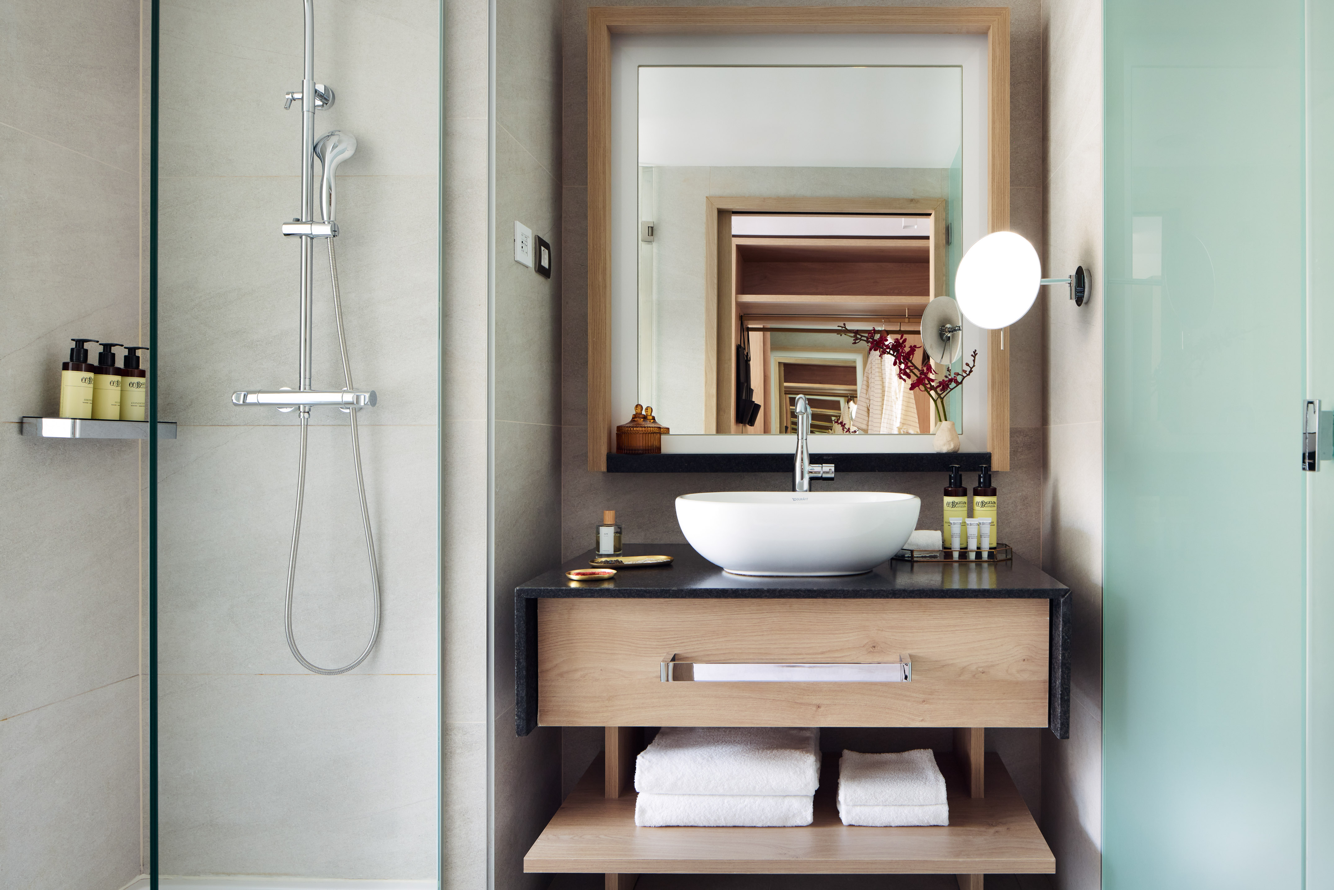 Modern bathroom with shower, vanity, vessel sink, wood mirror, and folded towels.