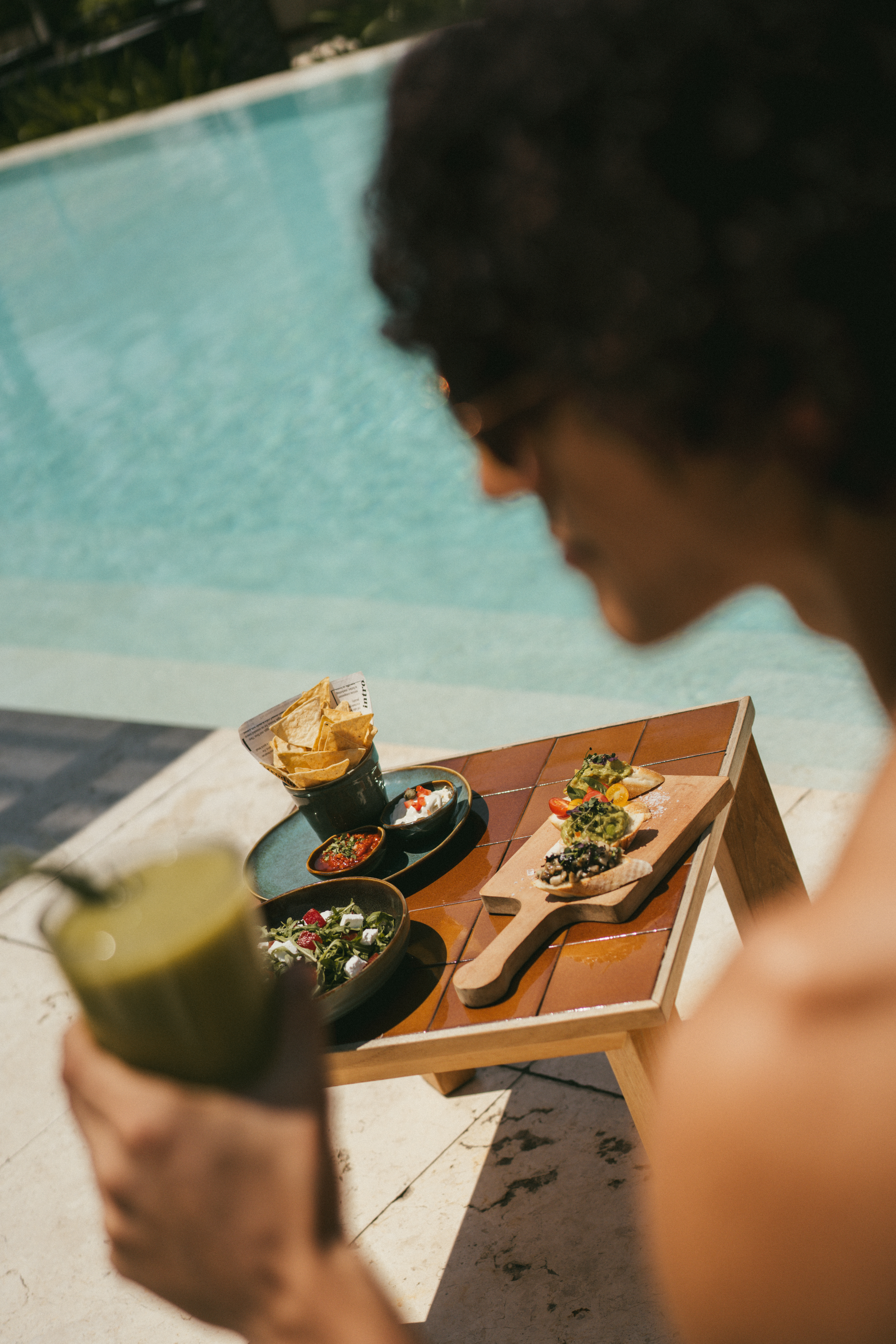 Healthy poolside meal with bruschetta, chips, salad, and green smoothie.