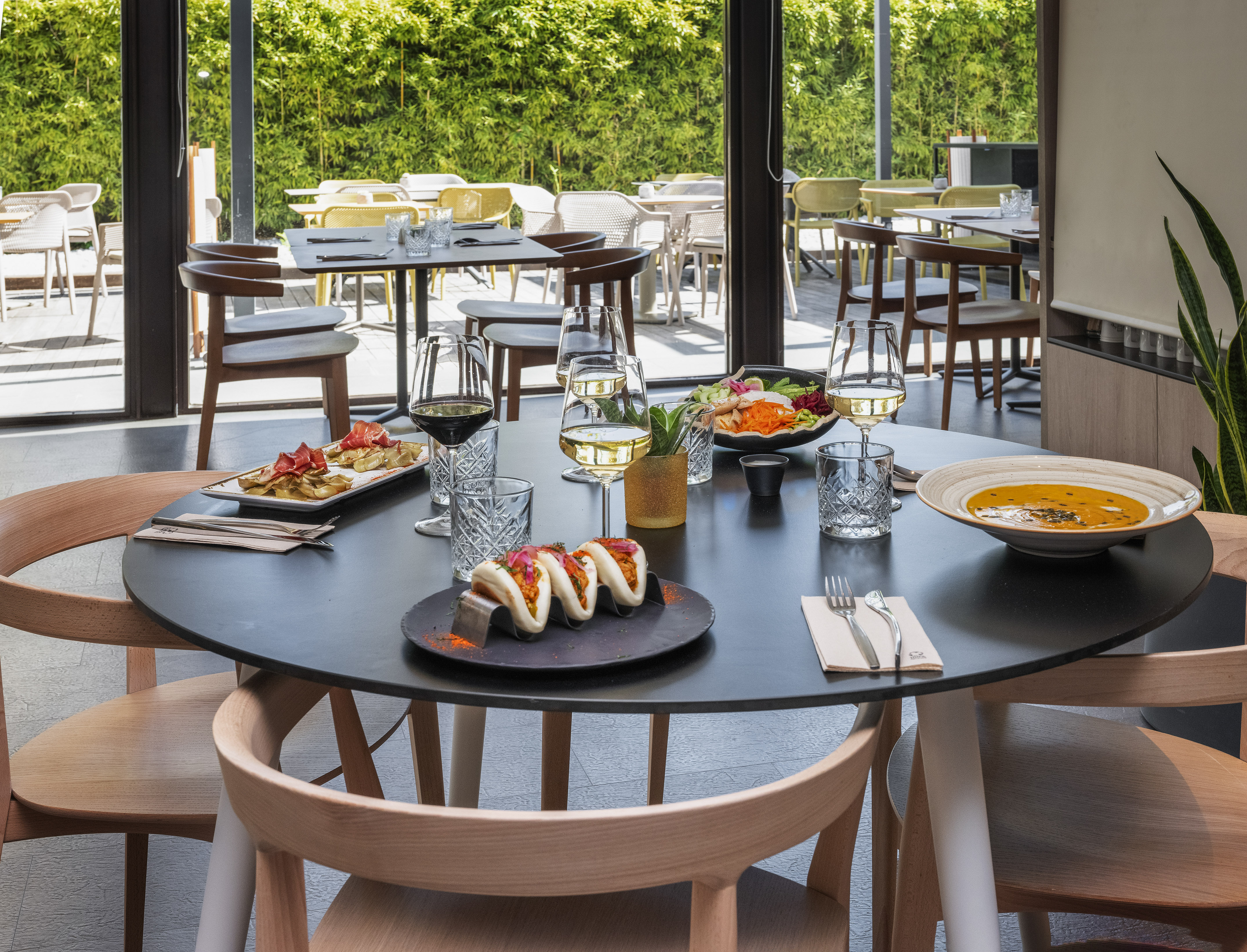 Modern restaurant table with bao buns, soup, wine, and patio view.