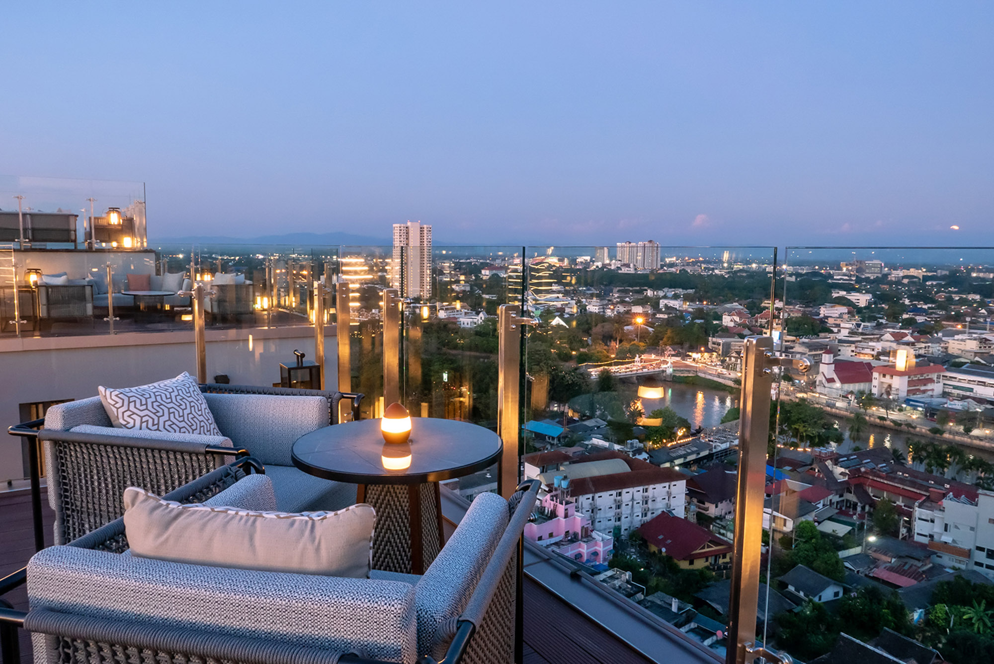 Modern rooftop bar with lounge seating overlooking a city at dusk.