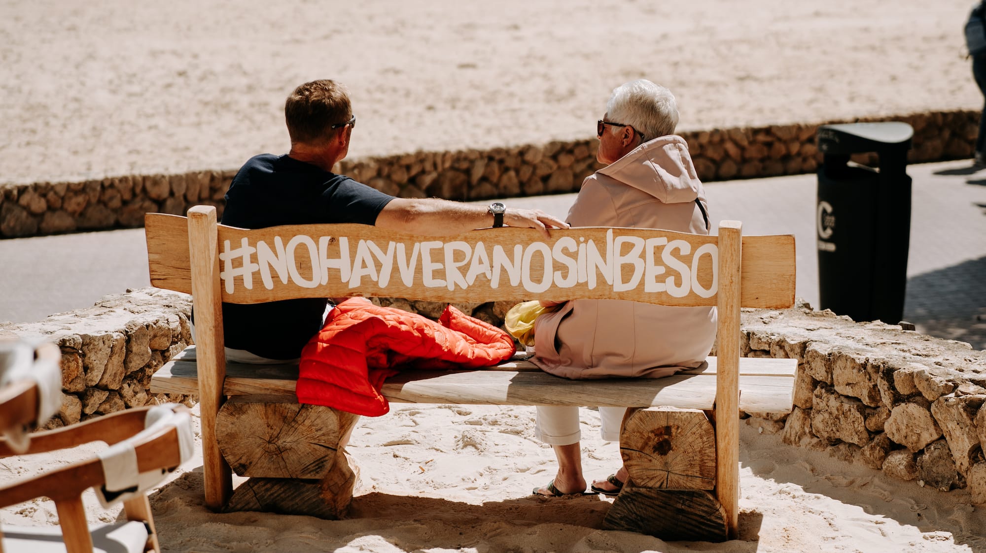 a man and woman sitting on a bench on a beach