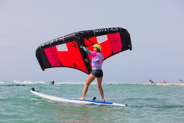 a woman on a surfboard with a red and black sail