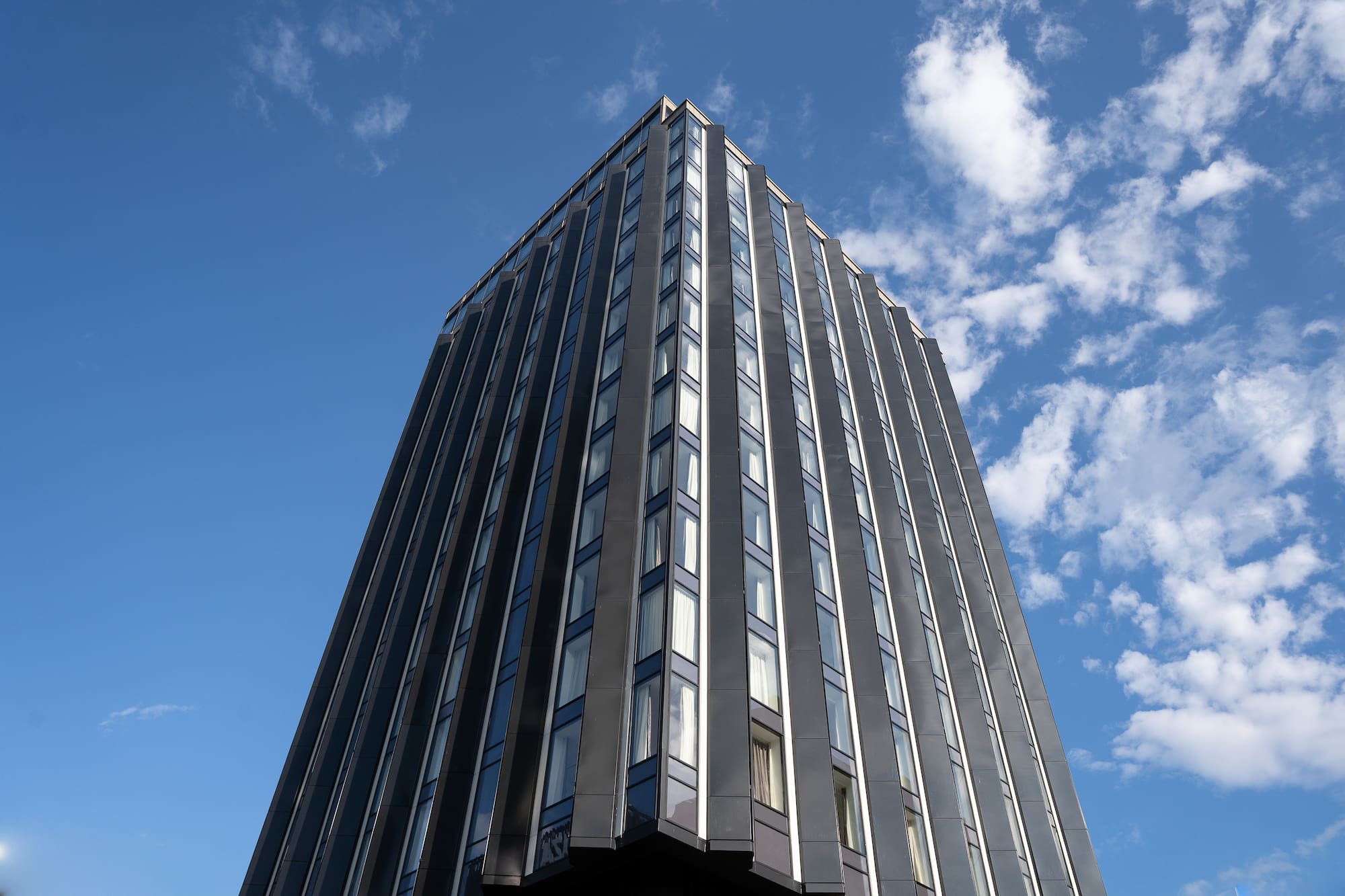 Upward view of a sleek, modern skyscraper with reflective glass and blue sky.