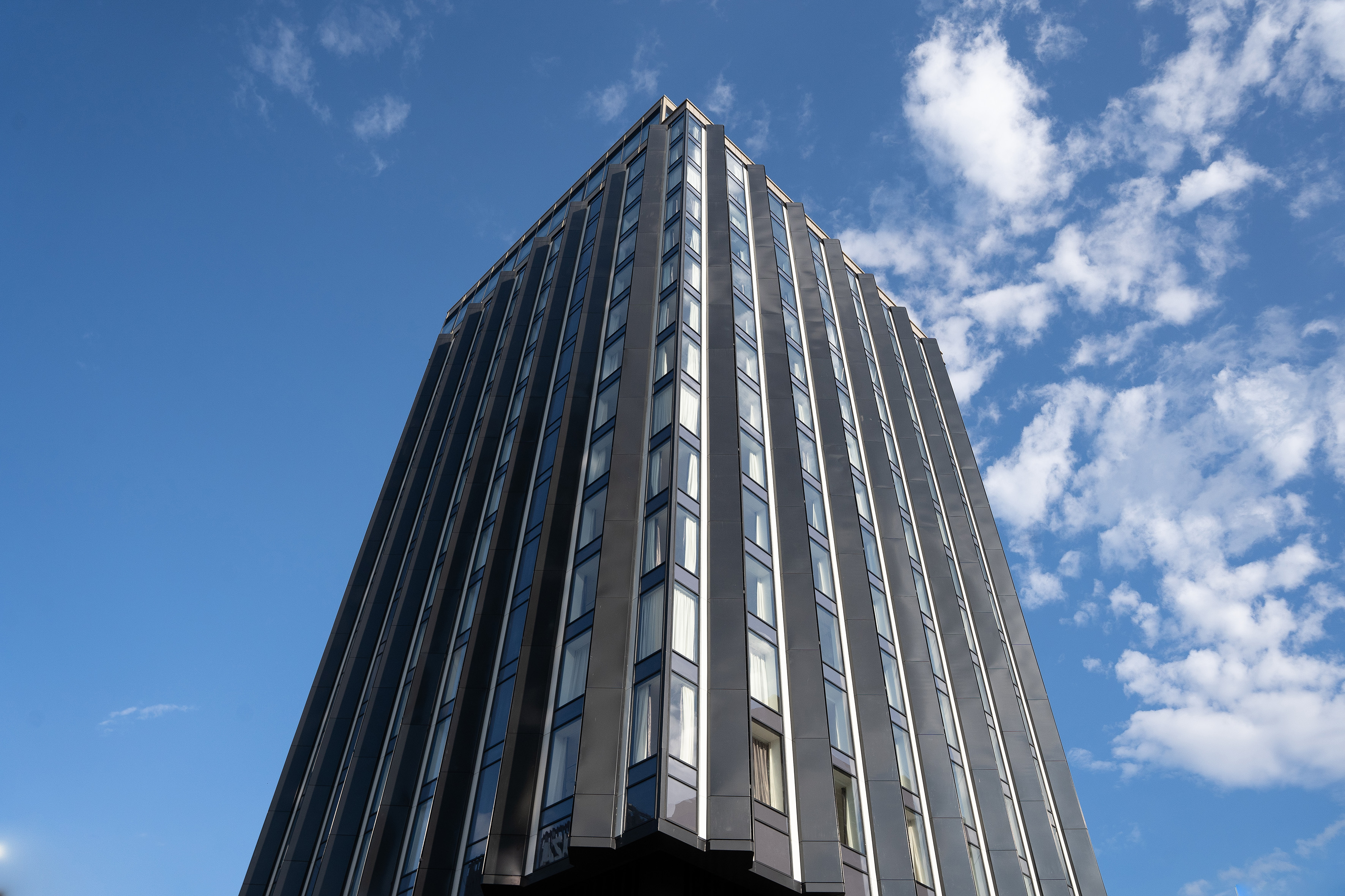 Upward view of a sleek, modern skyscraper with reflective glass and blue sky.