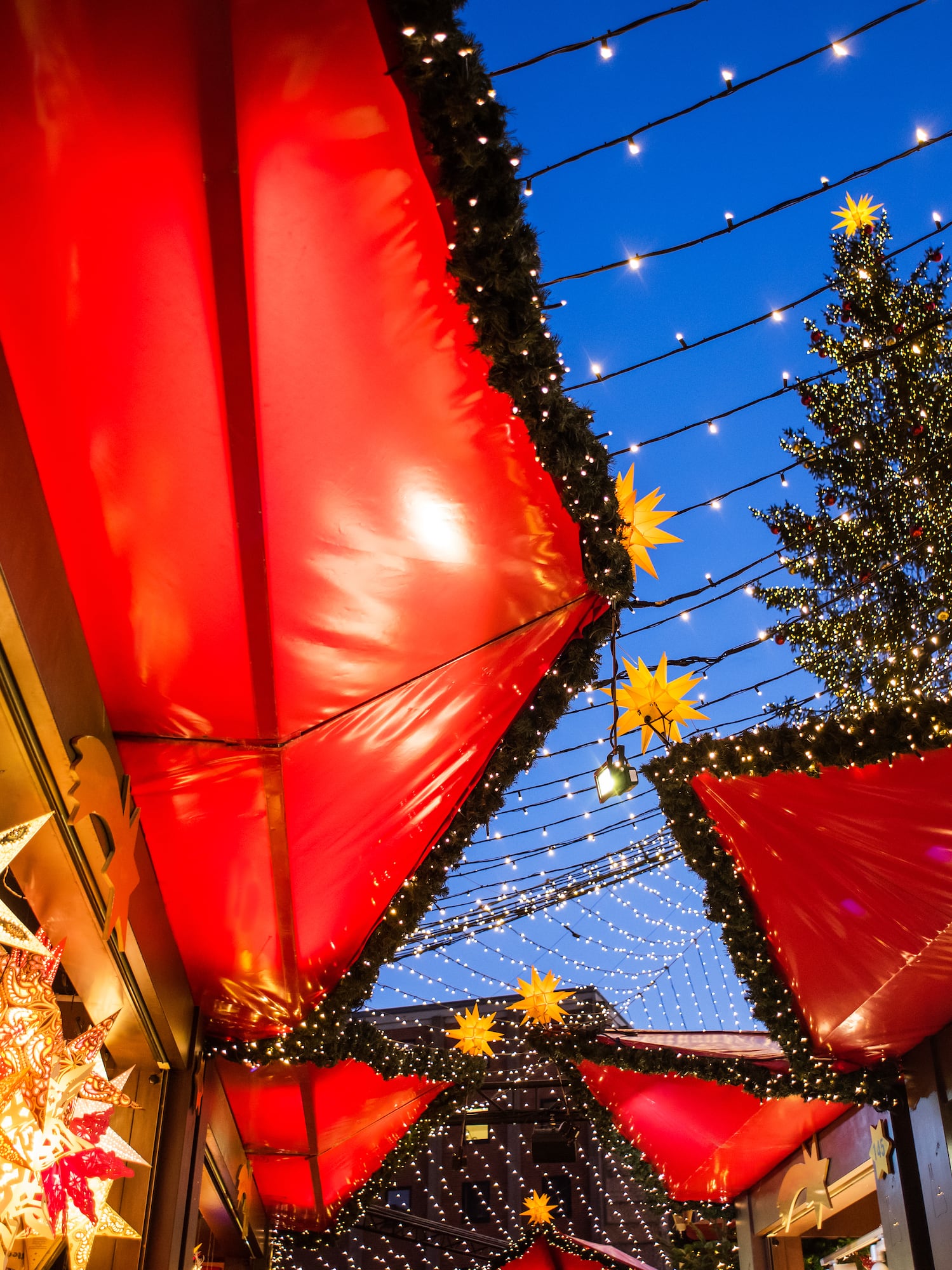 Festive Christmas market with red awnings, string lights, and decorated tree.