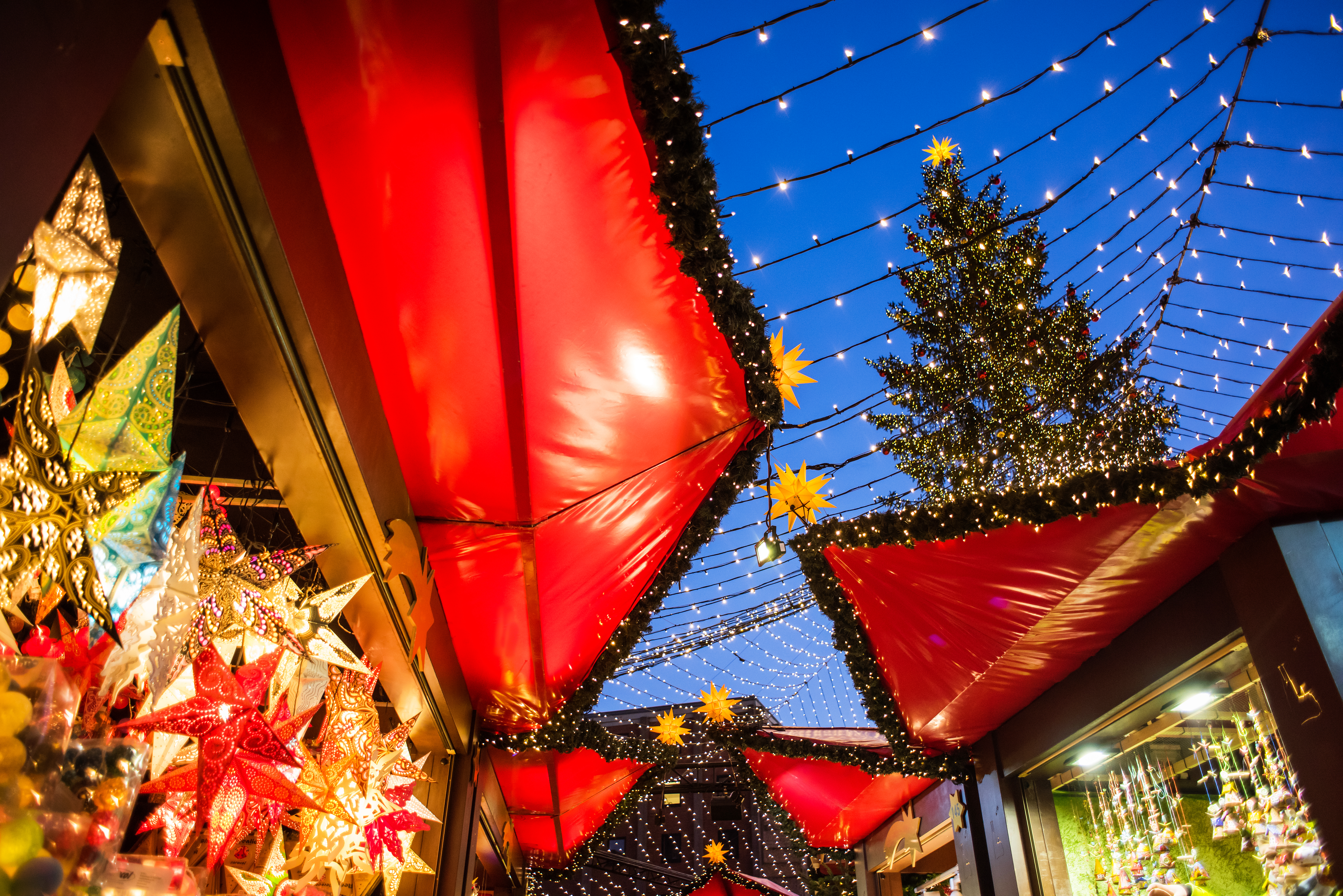 Festive Christmas market with red awnings, string lights, and decorated tree.