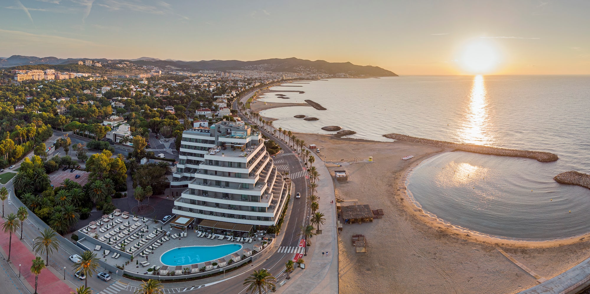 Hotel moderno con piscina en playa mediterránea al atardecer. Vista aérea.