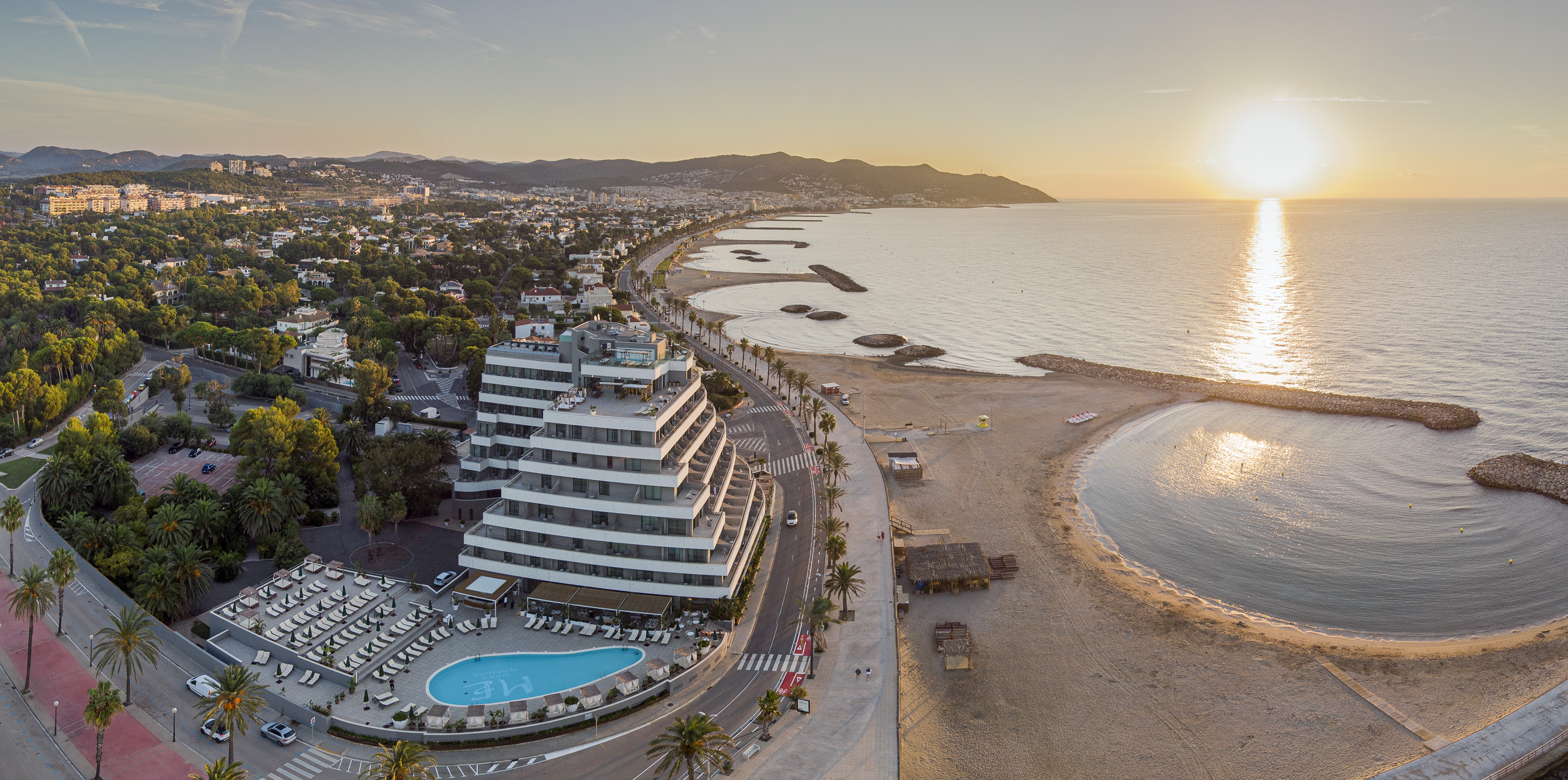 Hotel moderno con piscina en playa mediterránea al atardecer. Vista aérea.