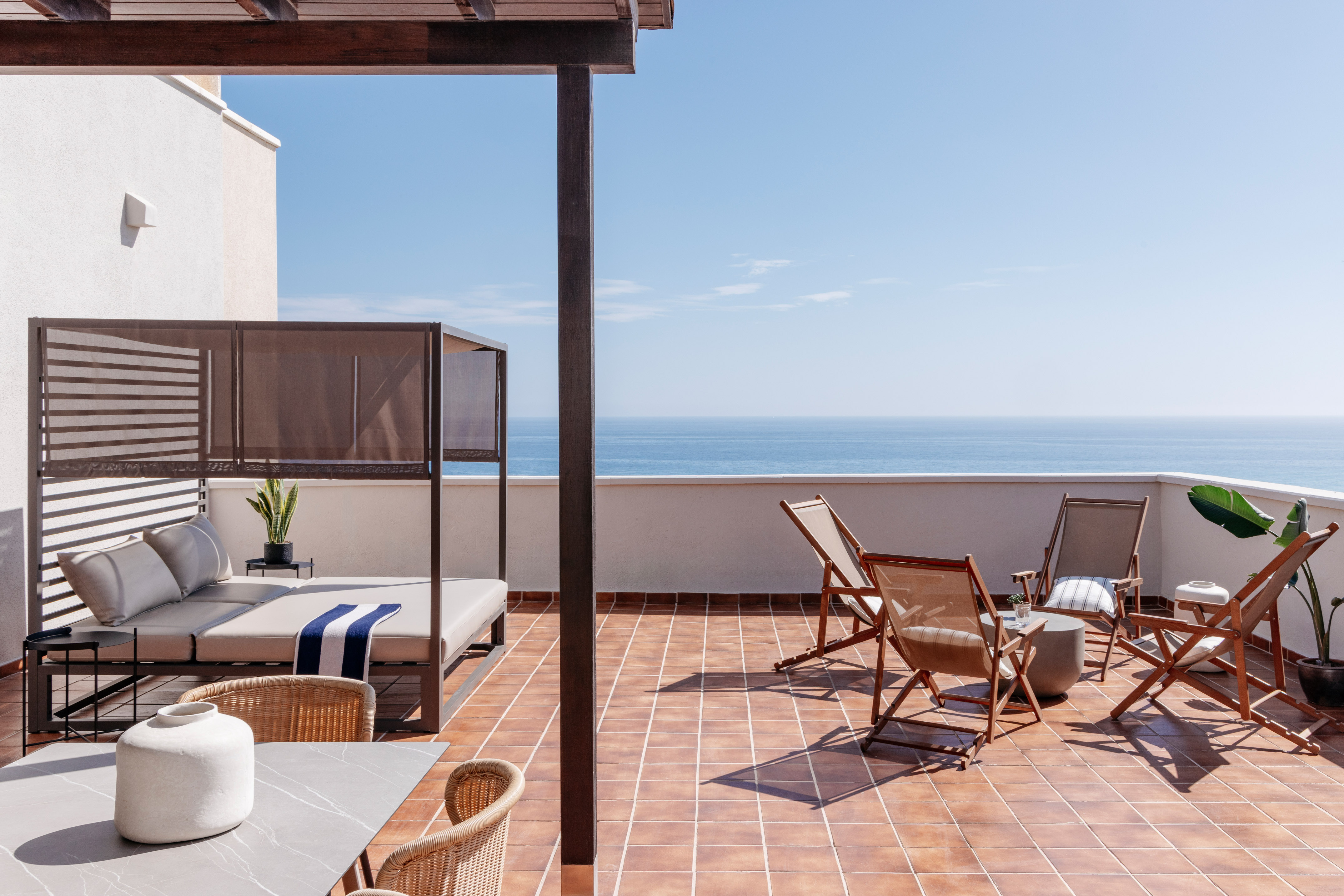 Sunny outdoor terrace with ocean view, daybed, pergola, and lounge chairs.