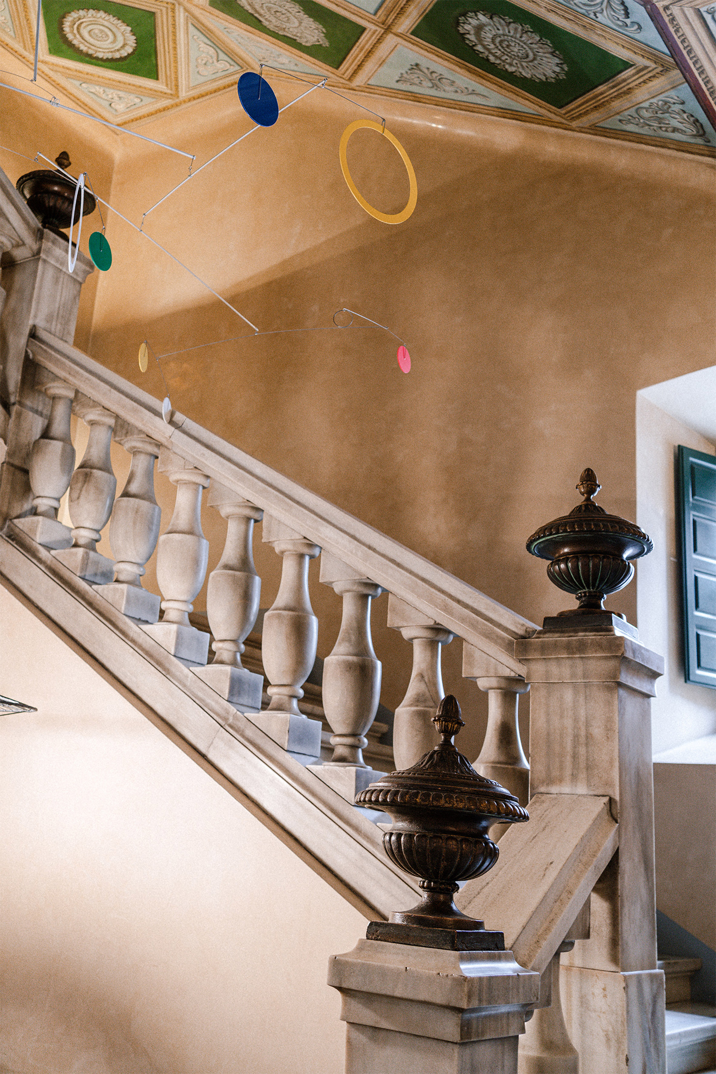 Marble staircase, ornate ceiling, modern mobile art with colorful discs.