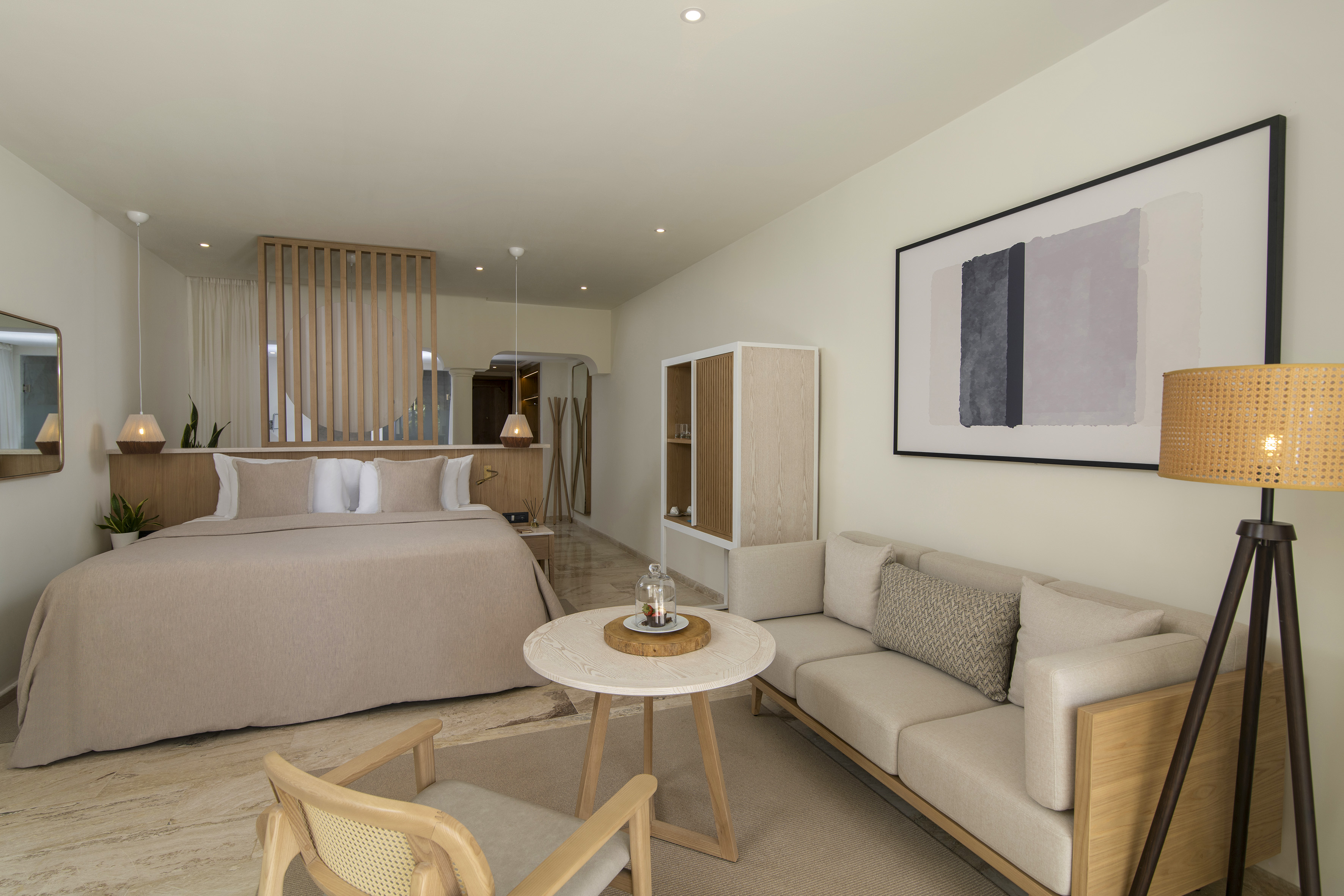 Neutral modern hotel suite with bed, sofa, wood screen, and minimalist design.