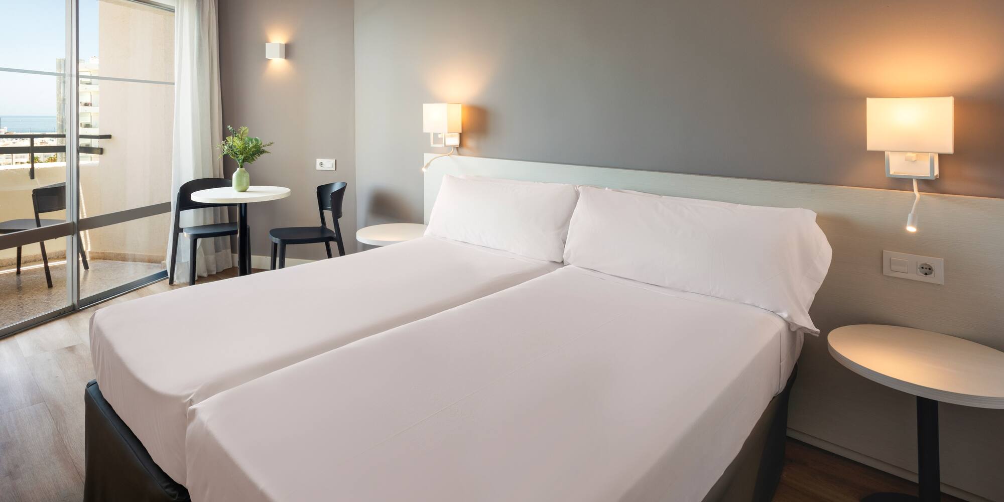 a bed with white sheets and a table with chairs and a lamp