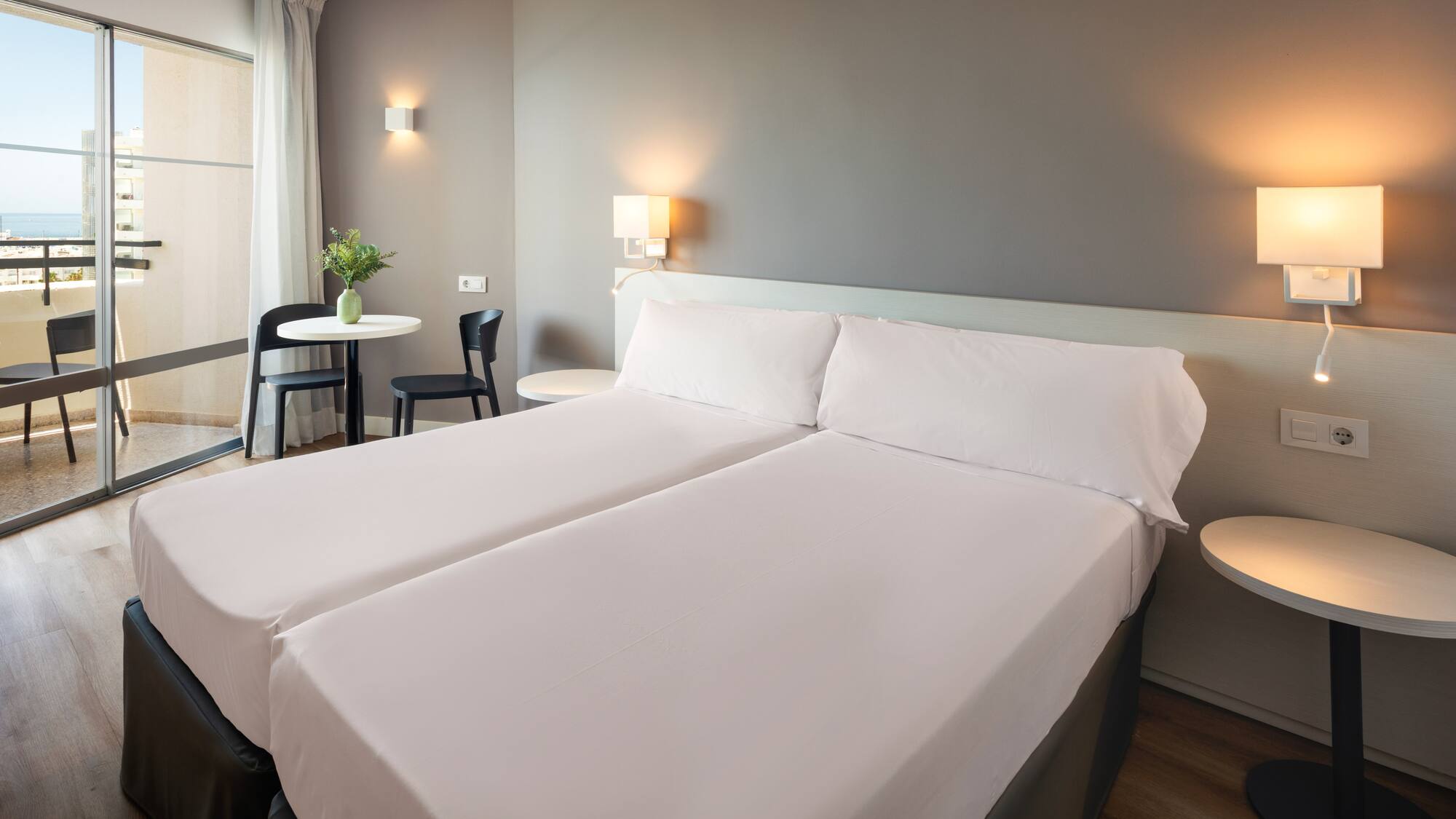 a bed with white sheets and a table with chairs and a lamp